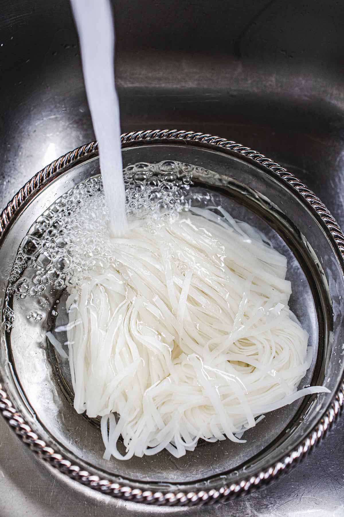 rinsing pad thai noodles in a glass bowl