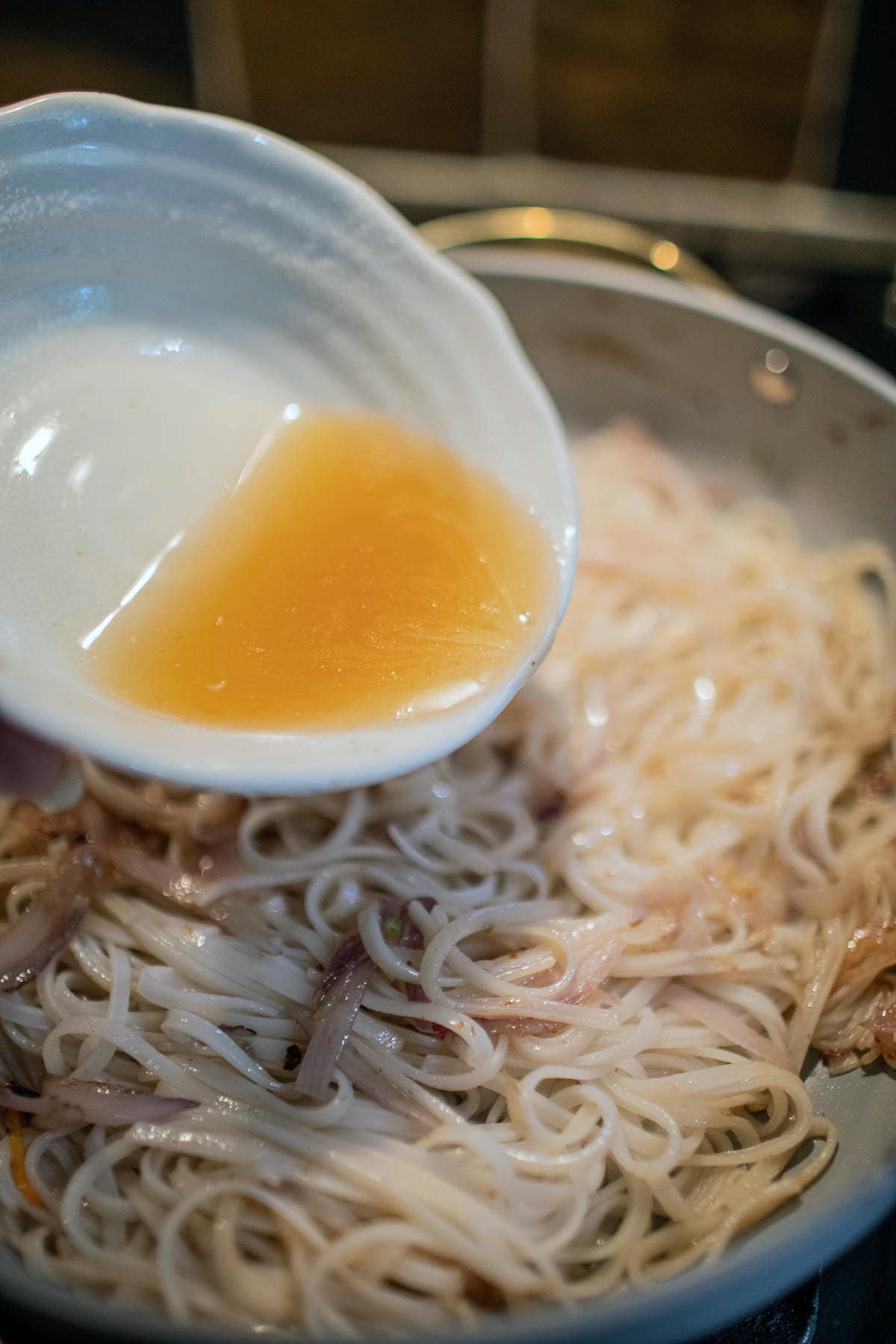 pouring pad thai sauce over noodles 