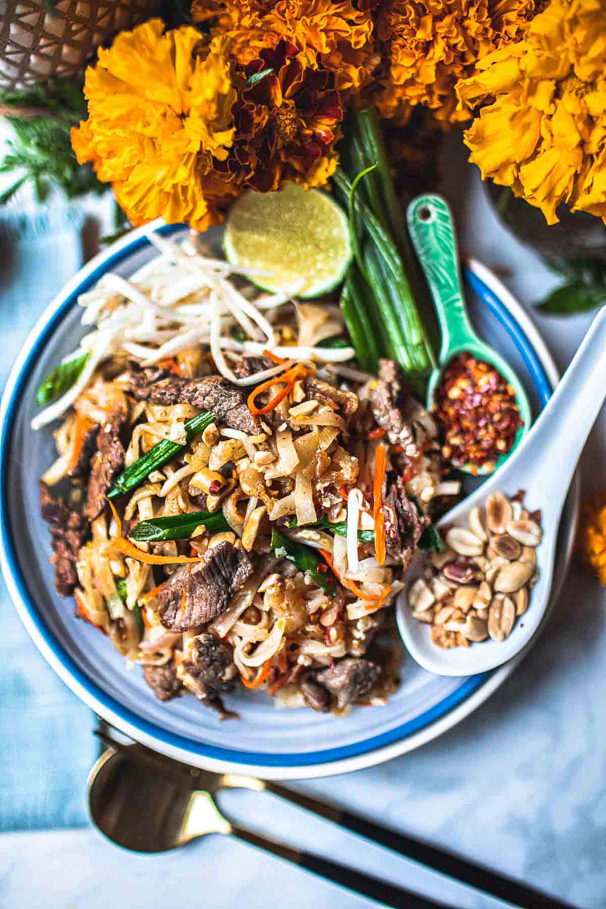 beef pad thai on a plate with peanuts and chili flakes garnish