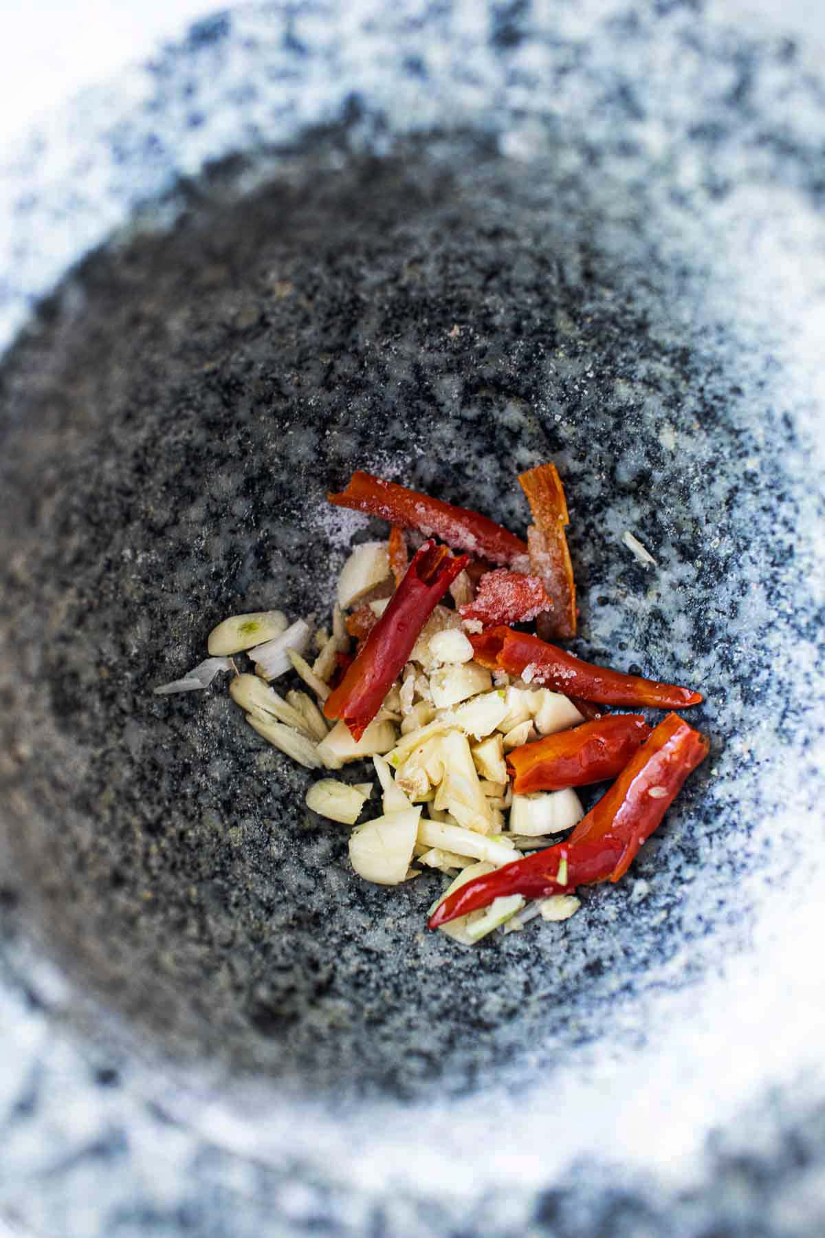 chilis, garlic and salt in stone mortar for making curry paste