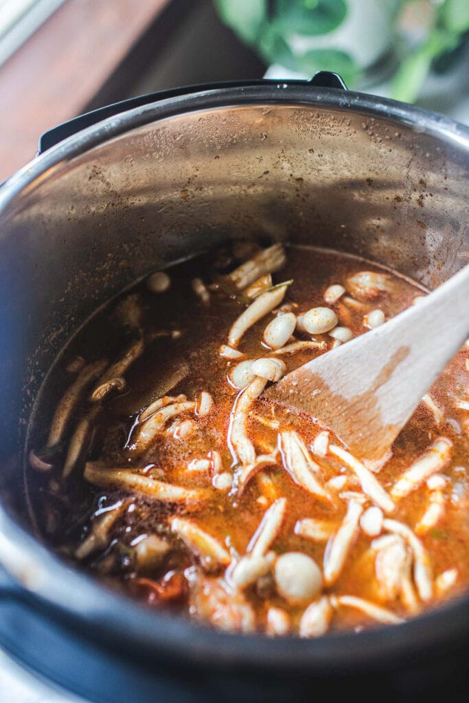 wooden spoon stirring tom yum soup in an instant pot