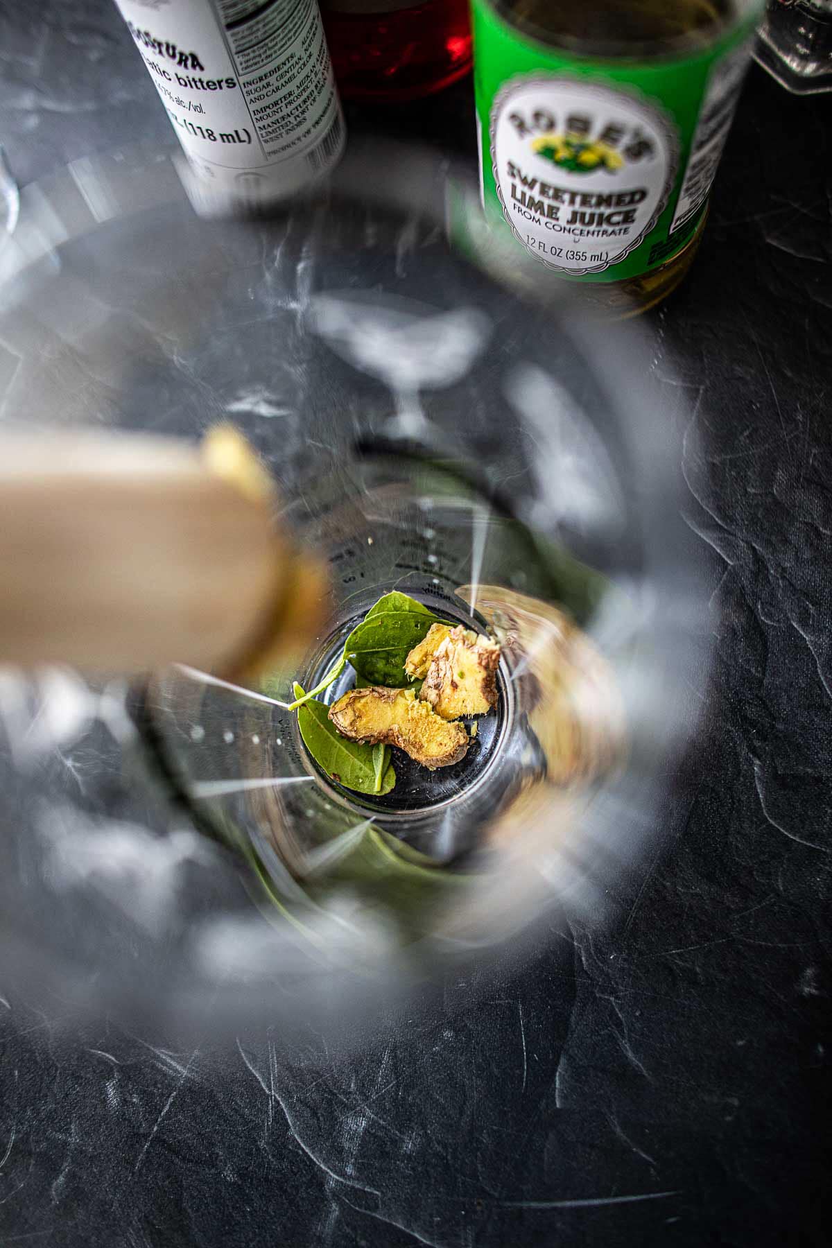 Muddling ginger and kaffir lime leaves in a shaker