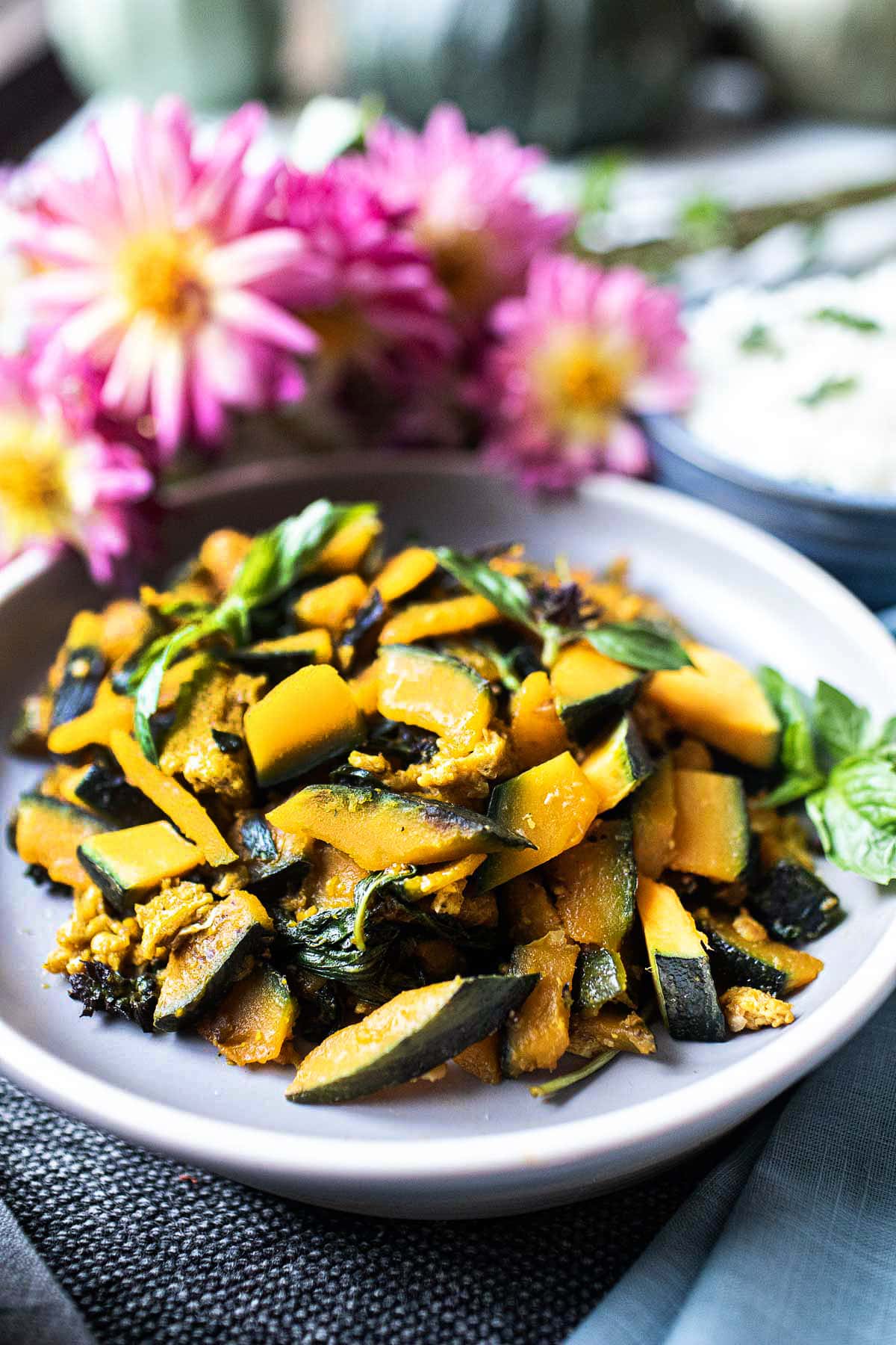 Thai kabocha squash stir fry on a gray plate near pink flowers