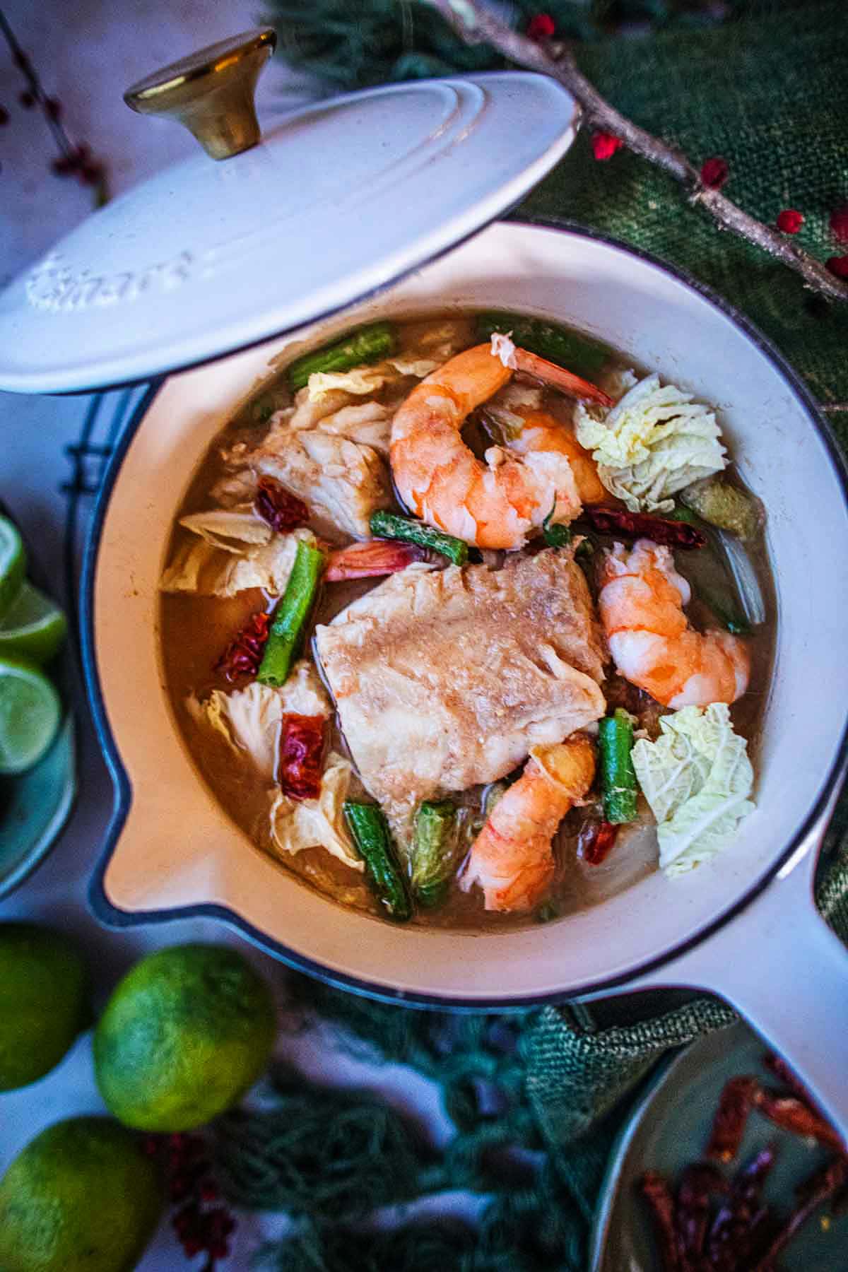 Thai sour curry soup with fish and shrimp in a white pot.