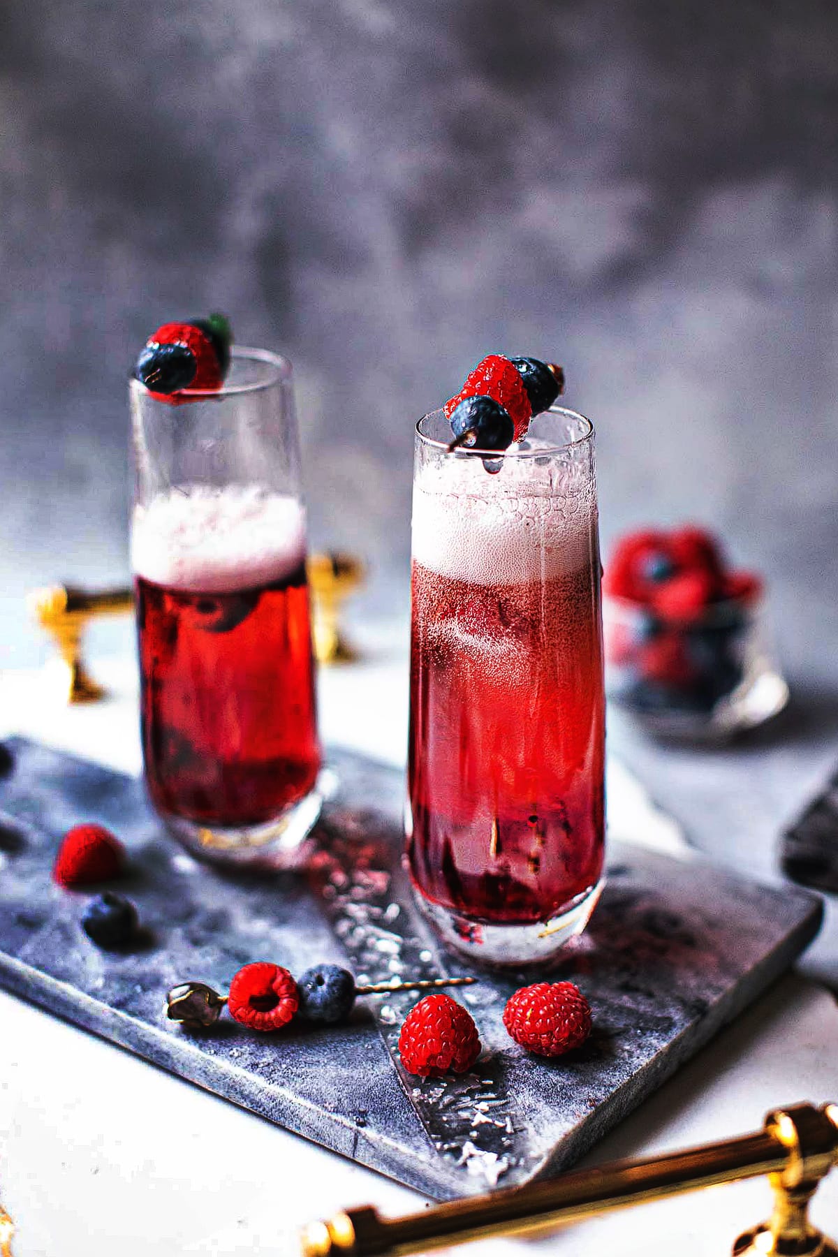 Kir Royale Cocktail in champagne glasses with berries garnish.