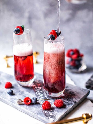 kir royale cocktail in 2 champagne glasses with berry garnish