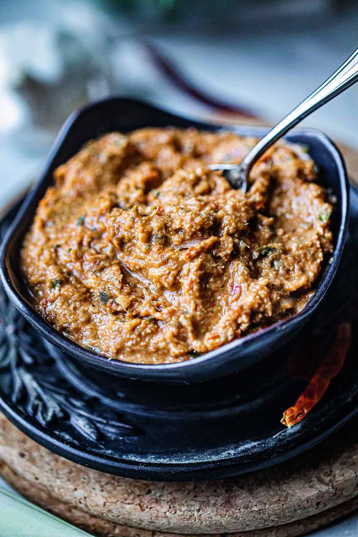 Tom Yum paste in a black bowl with a spoon dipped in the middle. 