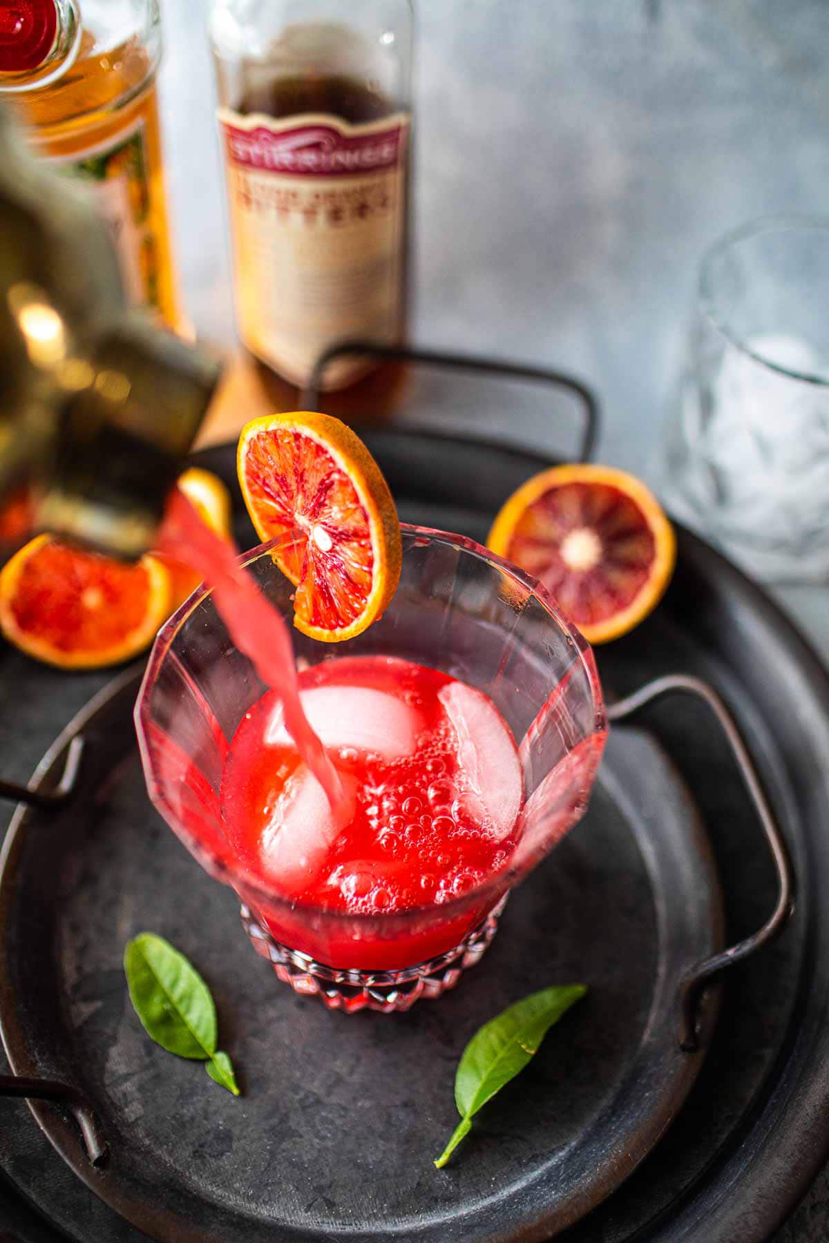 Pouring Tanqueray Sevilla orange cocktail into a glass with ice.
