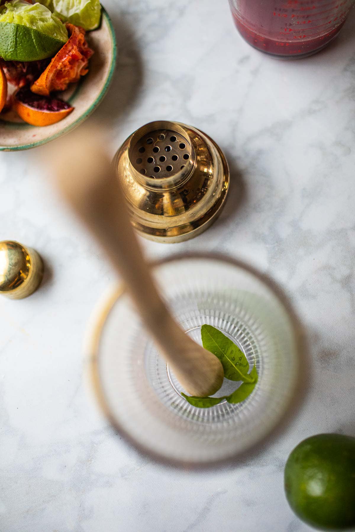 Kaffir lime leaves in a shaker with wooden muddler.