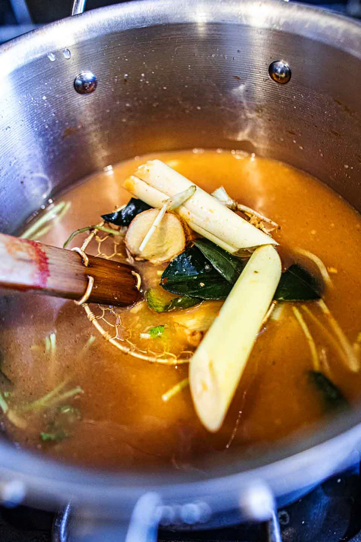 Adding aromatics to Tom Yum in a pot.