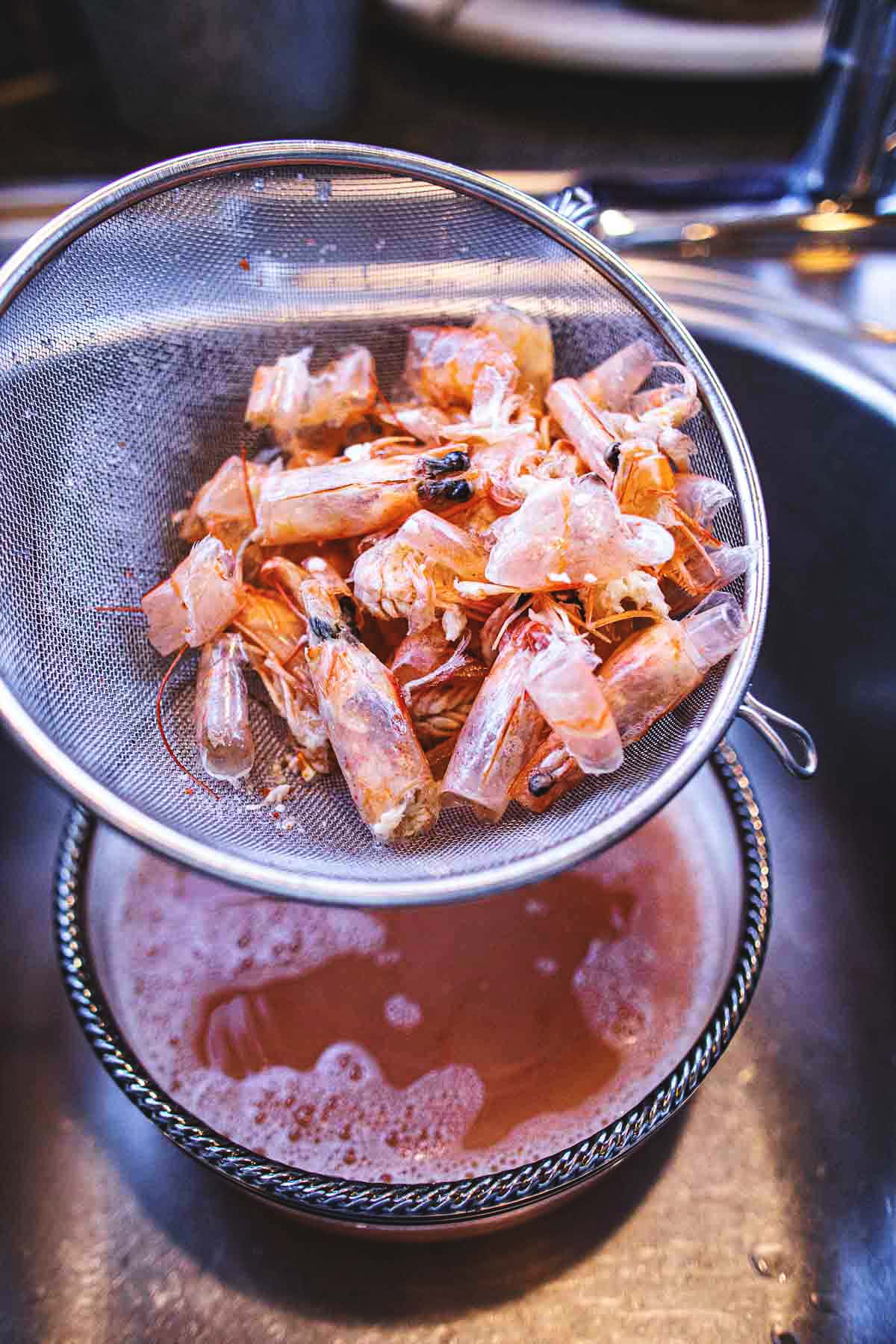 Straining Tom Yum broth and shrimp heads in a colander.