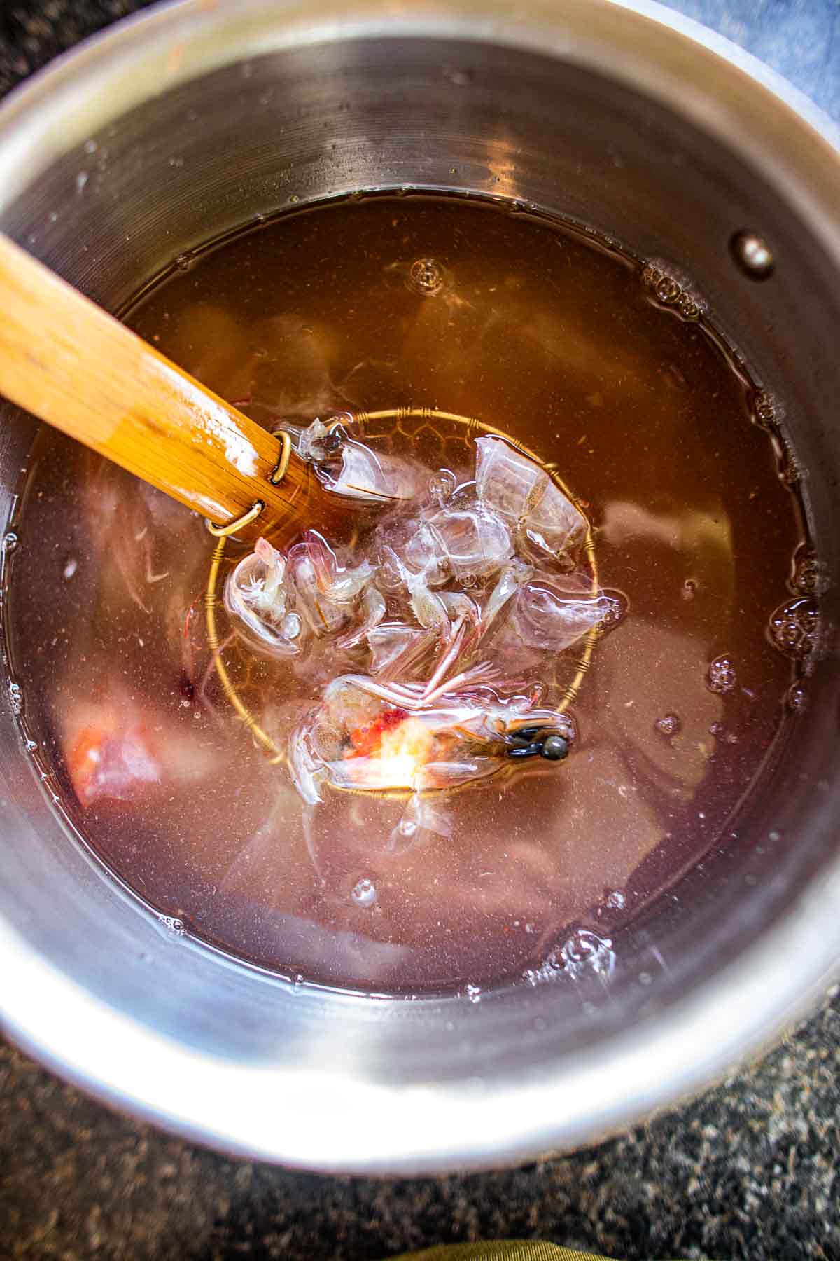 Adding prawn heads to a pot of broth.