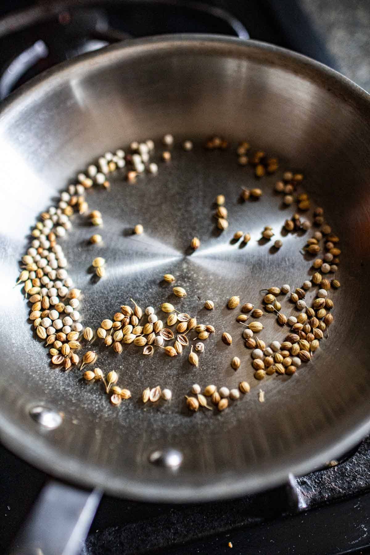 Toasted coriander and white peppercorns in a skillet.