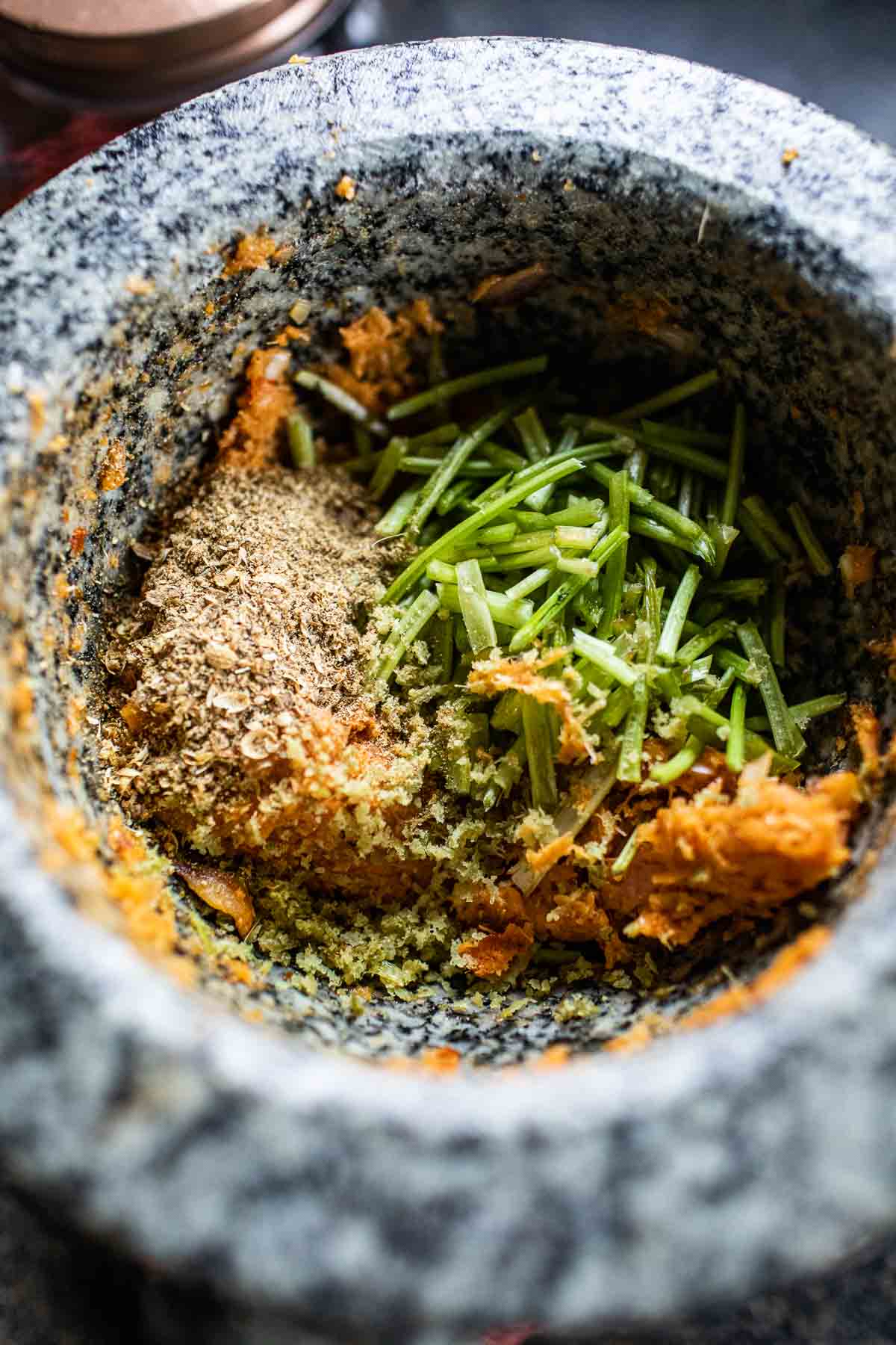 cilantro stems and spices in tom yum paste in a mortar.