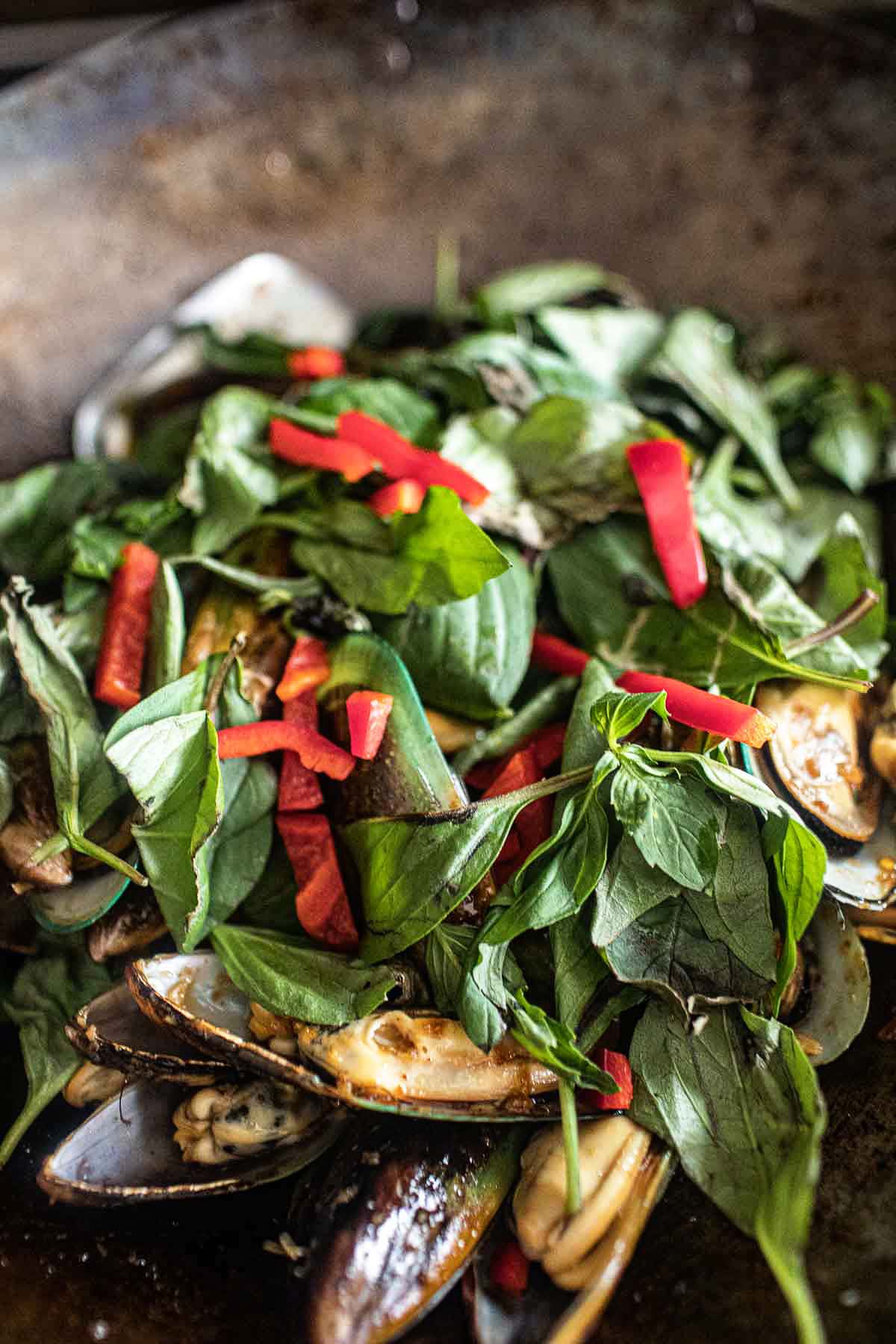 Thai Spicy mussels stir fry with basil in a wok.