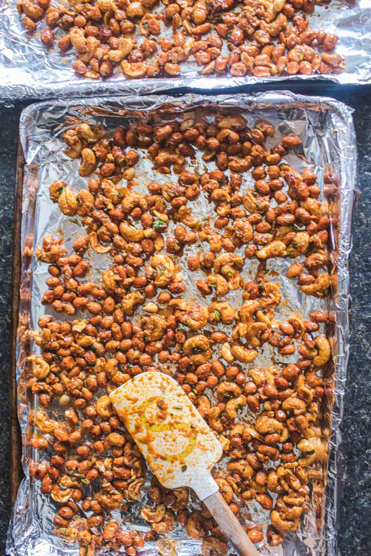 Tom yum roasted mixed nuts on a baking sheet with spatula.