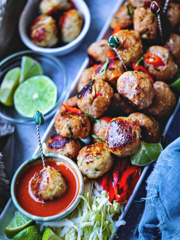 Tom yum meatballs on a platter with chili dipping sauce on a table.