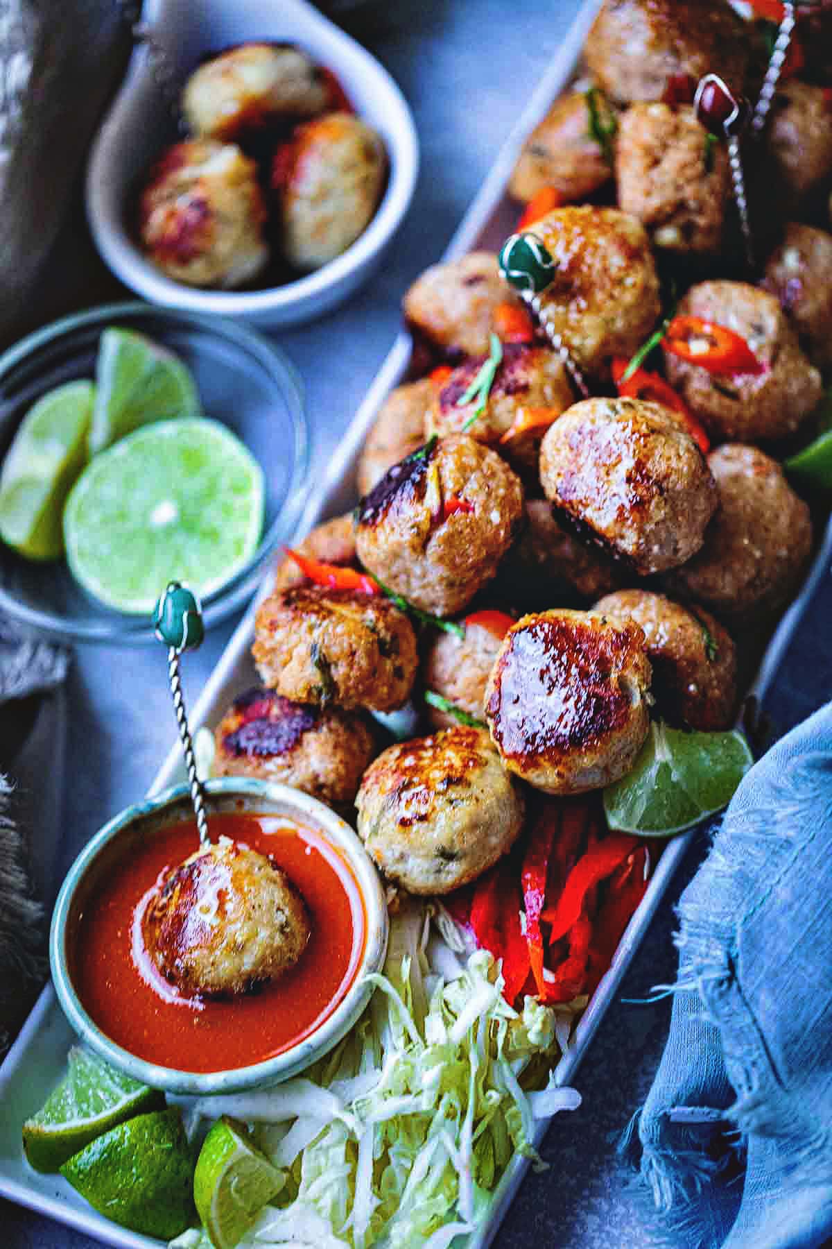 Tom yum meatballs on a platter with chili dipping sauce on a table.