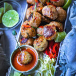 Thai meatballs on a platter with chili dipping sauce on a table.