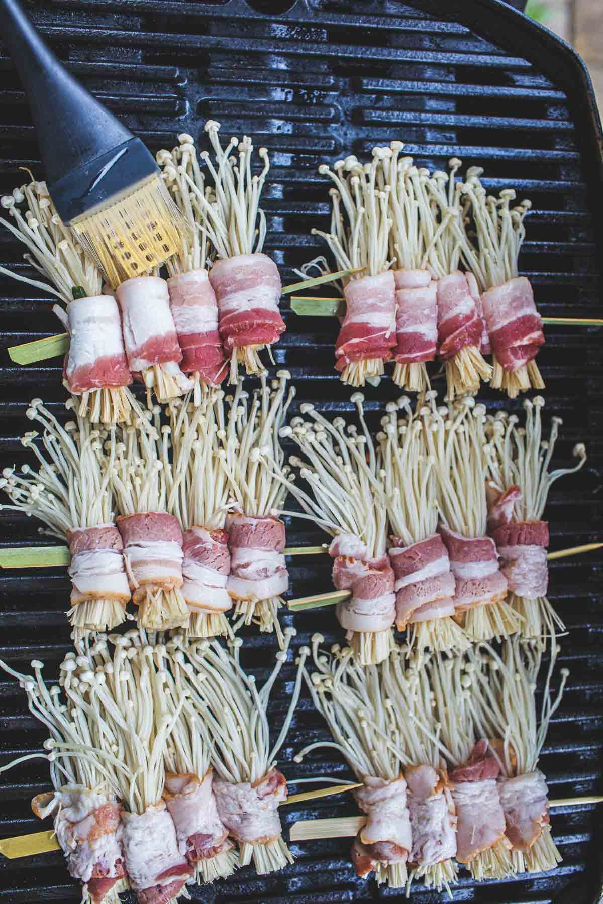 Enoki and bacon skewers on the grill with a brush on the mushrooms. 
