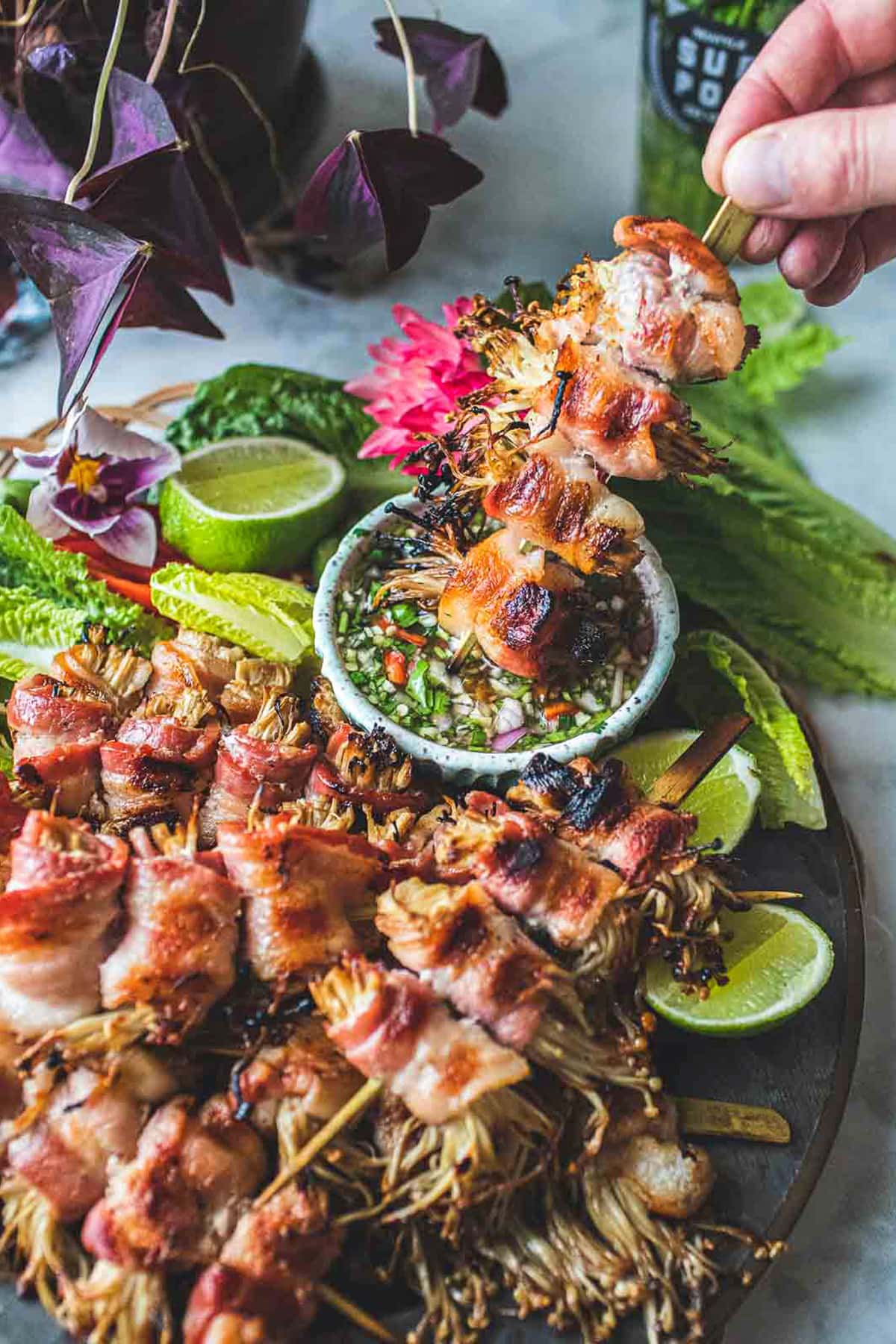 Enoki bacon on a skewer in a dipping sauce. 