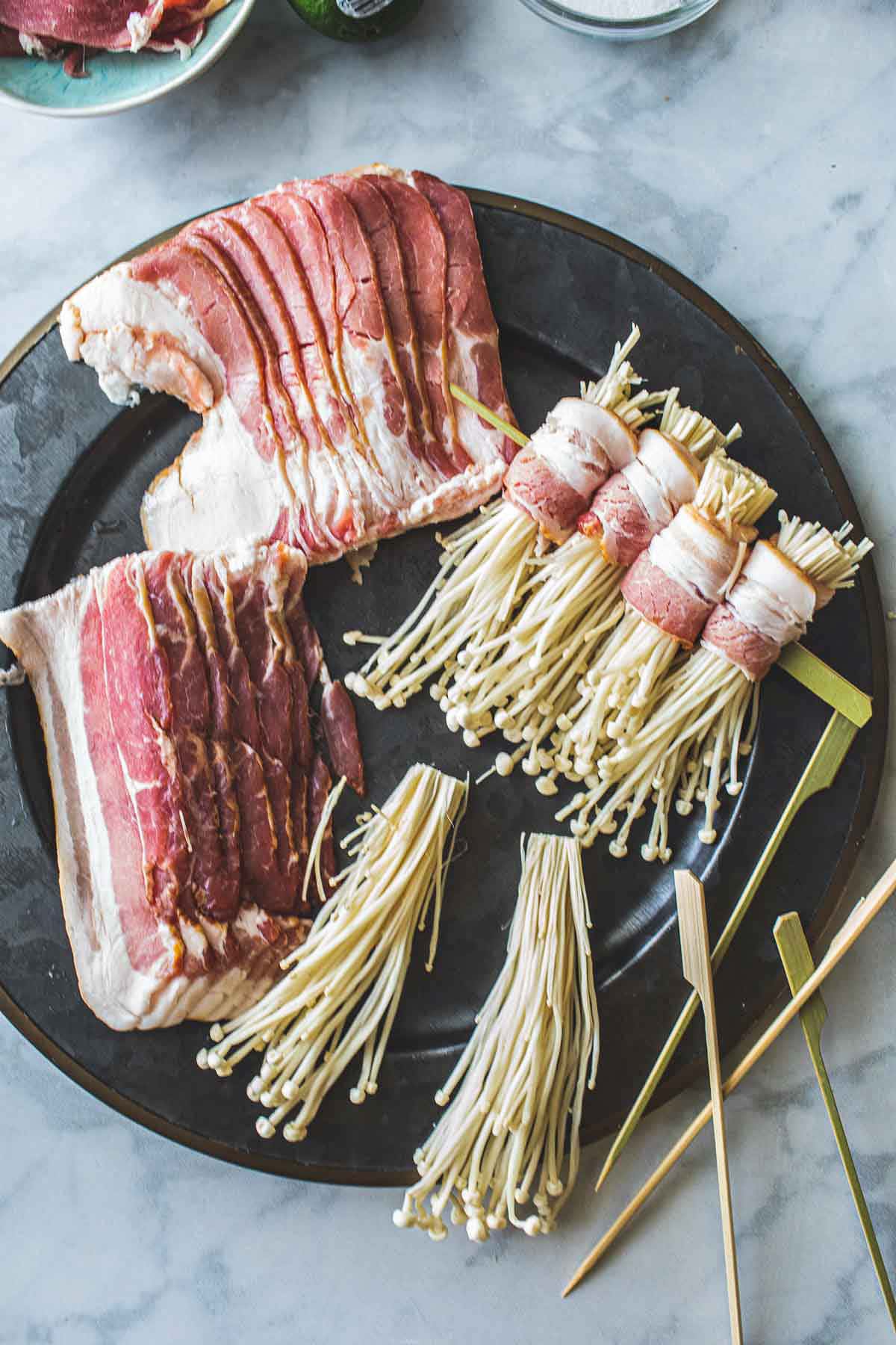 Enoki and bacon wrapped on skewers on a platter. 