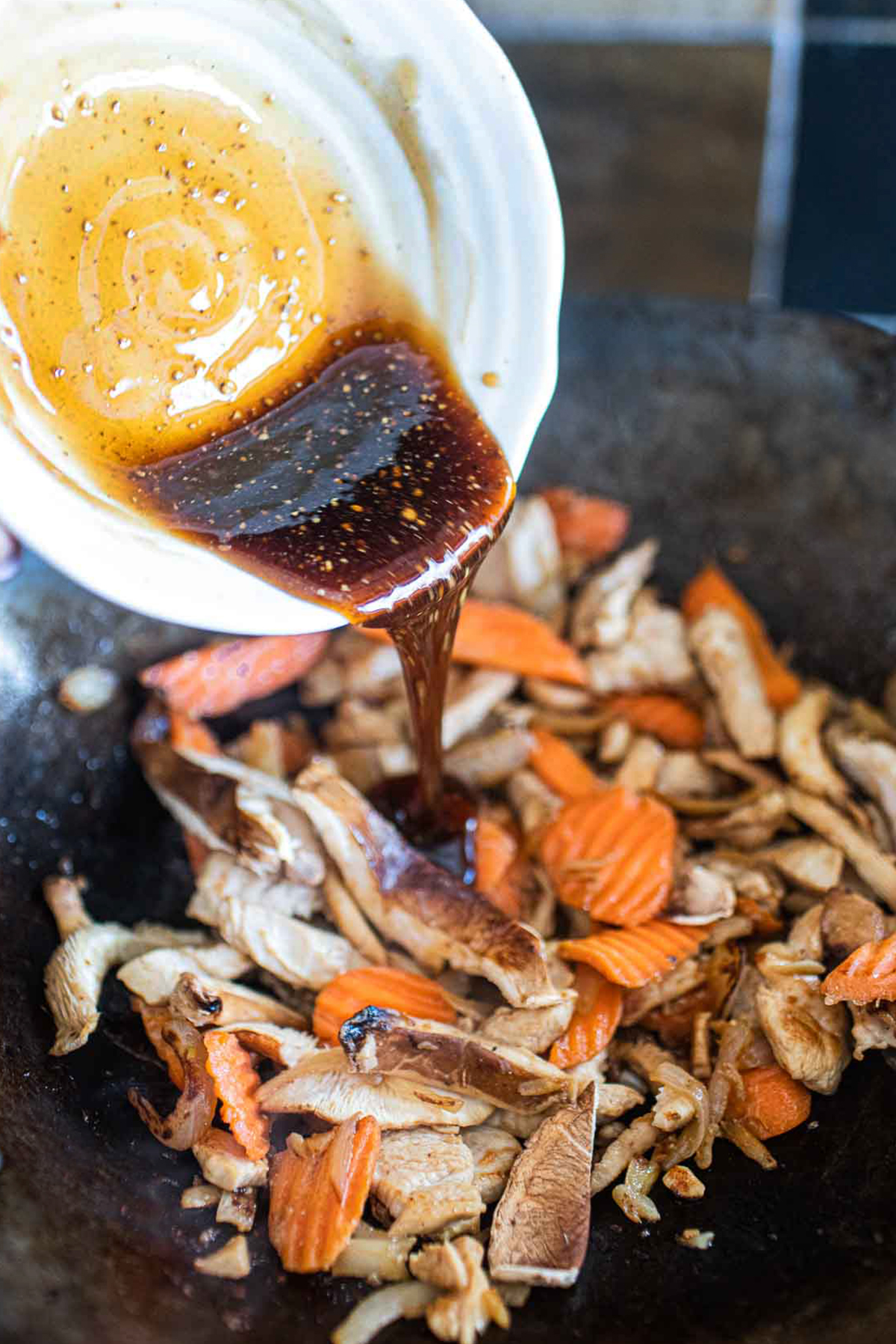 Sauce pouring into ginger chicken stir fry in a wok.