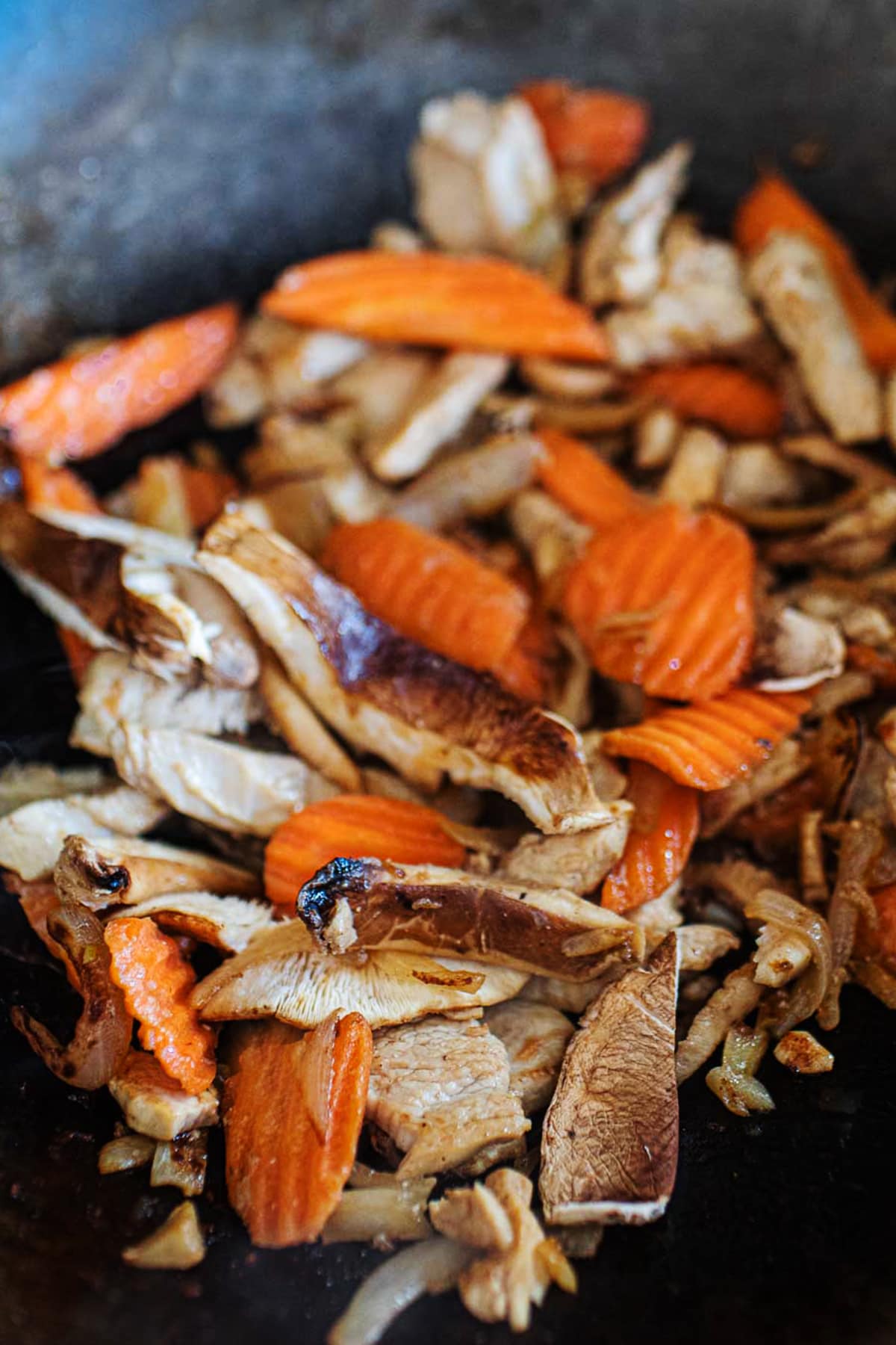 Carrot, mushrooms and chicken stir frying in a wok.