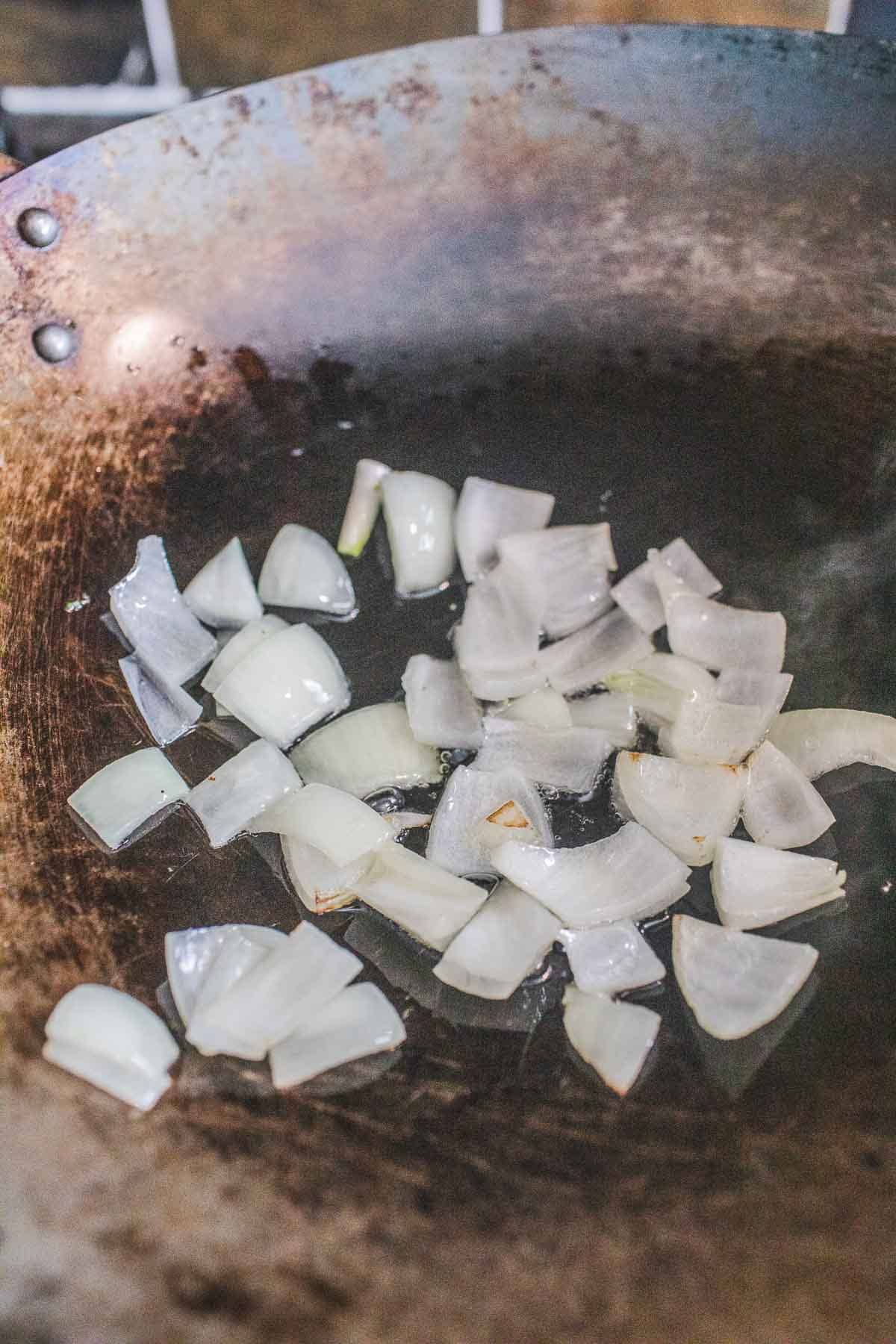 Onion pieces in a wok for making Thai mixed vegetable stir fry.