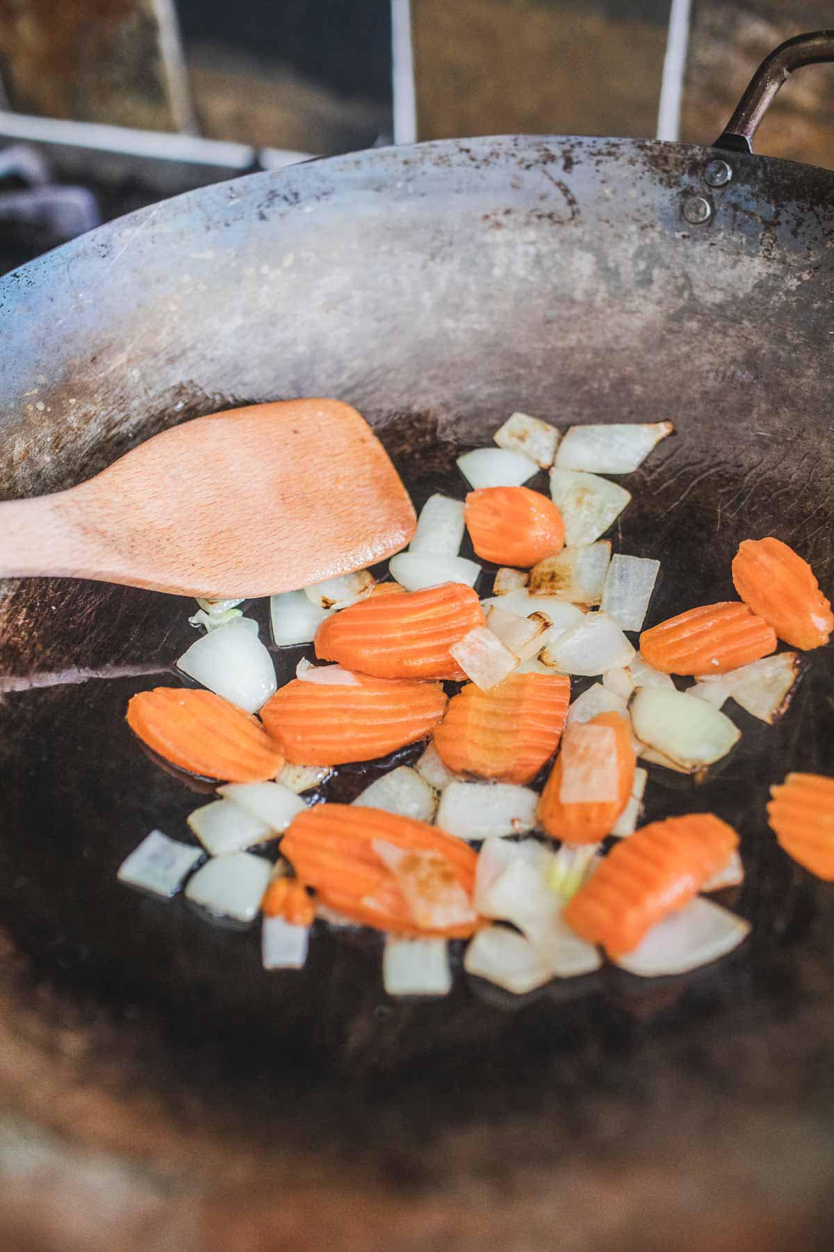 Onion and carrot pieces in a wok for making Thai mixed vegetable stir fry.