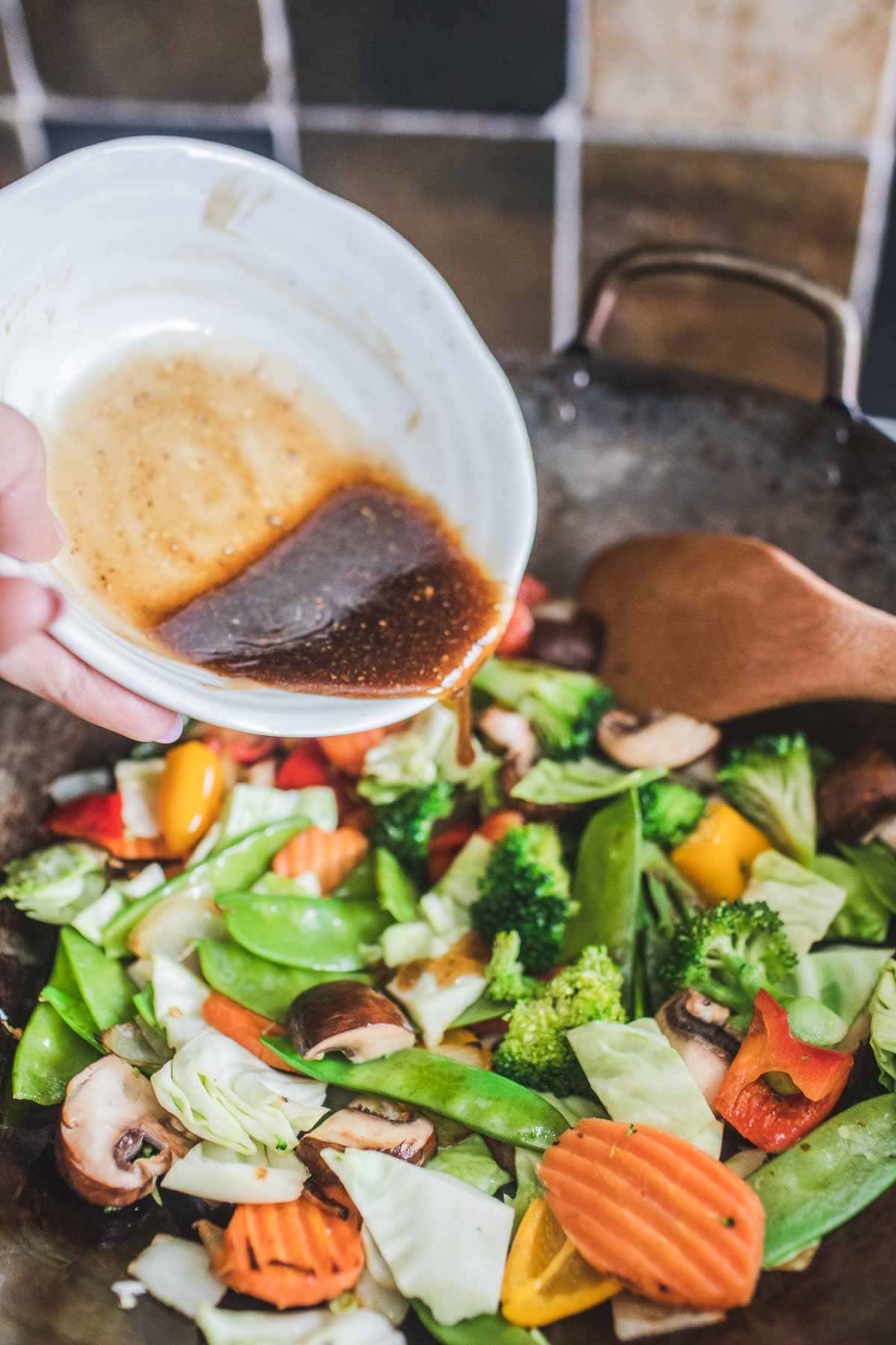 Sauce in a bowl pouring into Vegetables in a wok for making Pad Pad Room Mit stir fry.