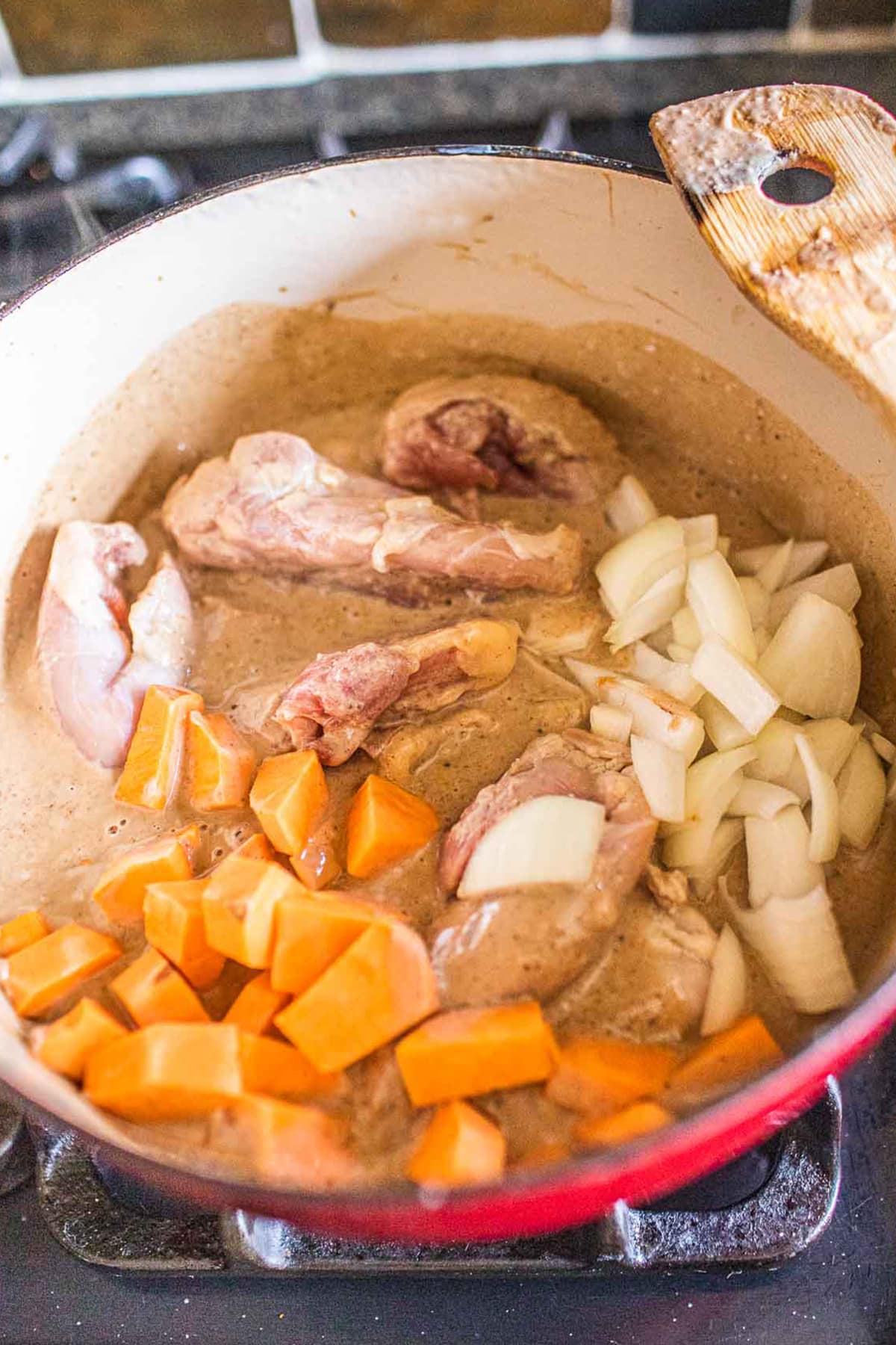 Potatoes, chicken and onion over massaman sauce in a pot.