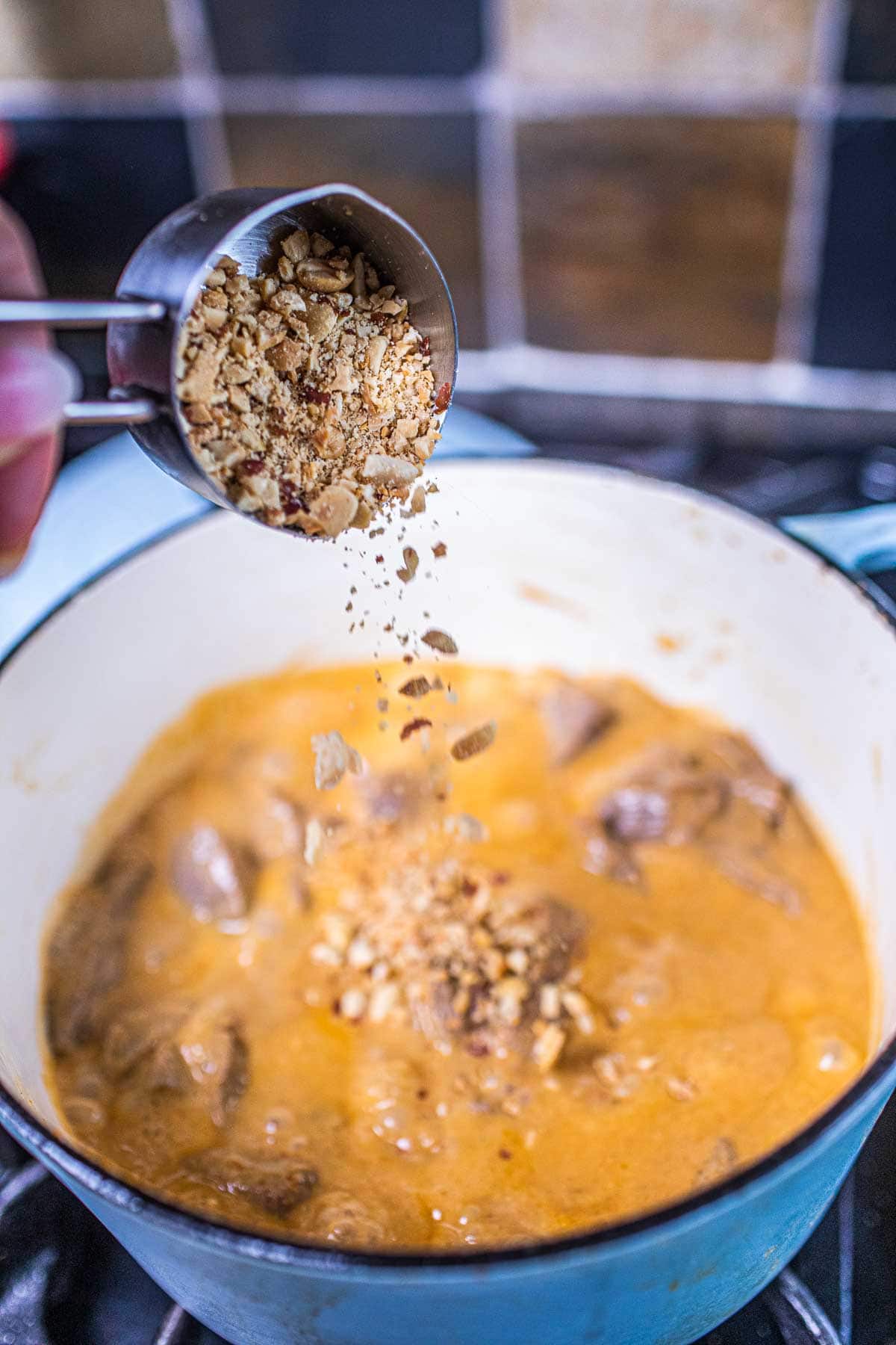 Panang curry with peanuts pouring into a pot of curry sauce. 