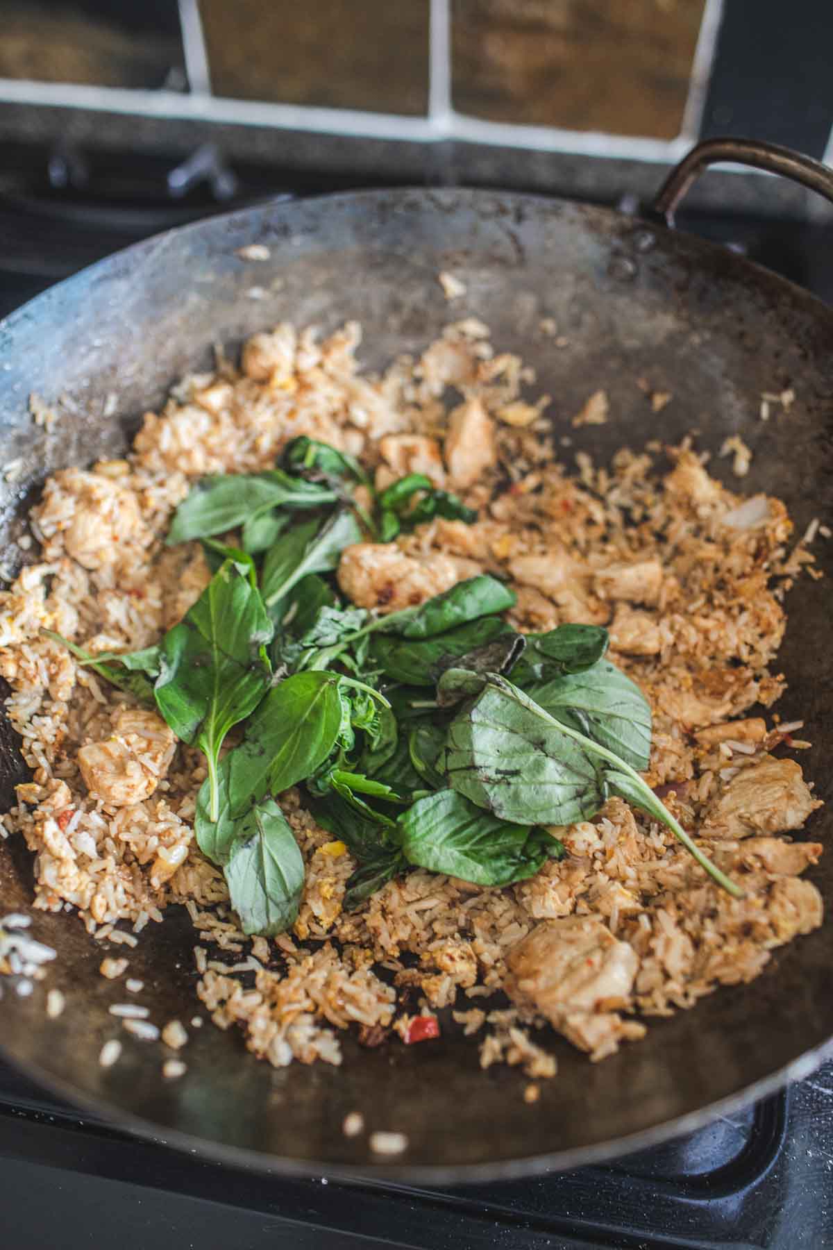 Thai chicken basil fried rice in a wok with fresh basil on top.