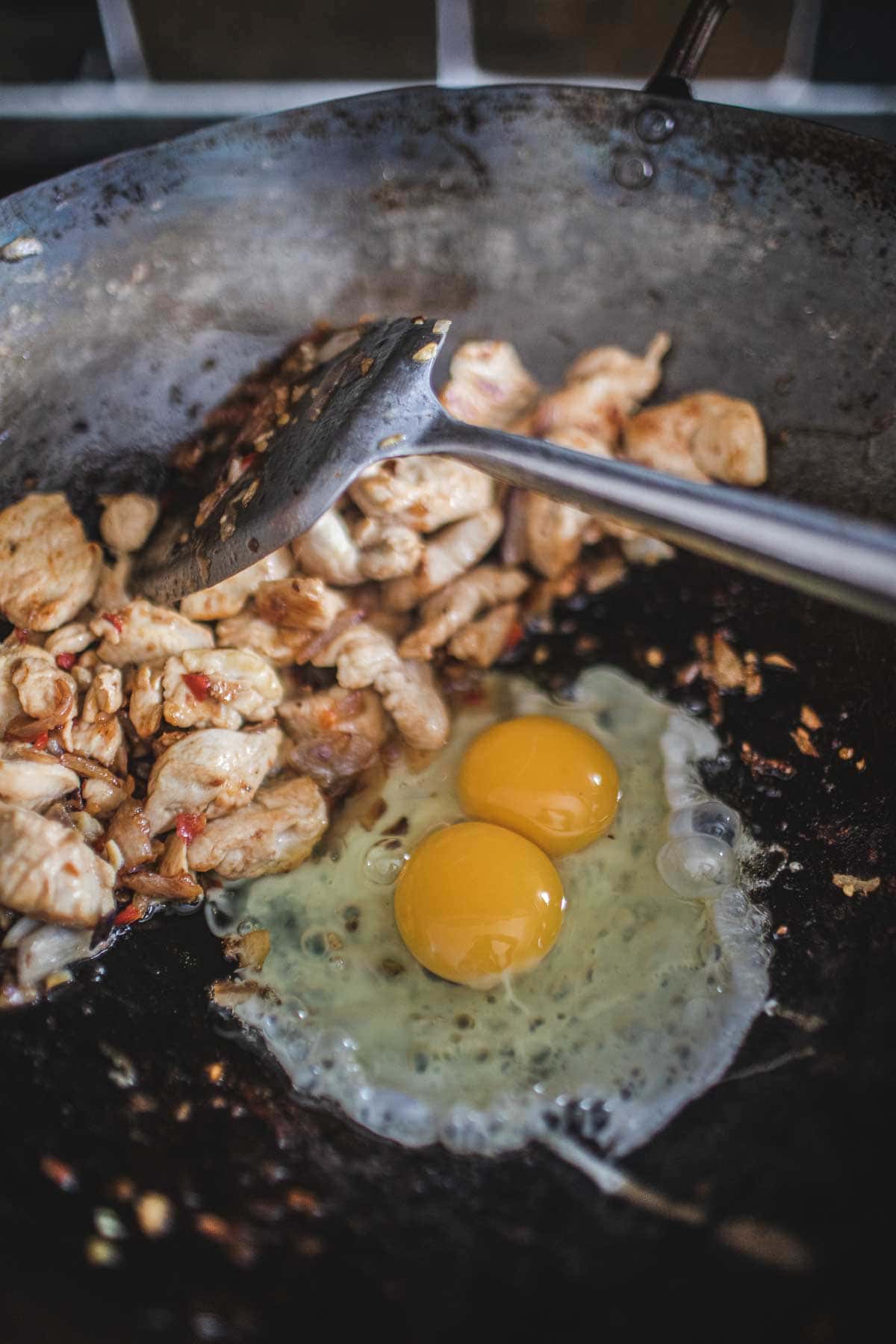 2 eggs frying next to chicken in a wok.