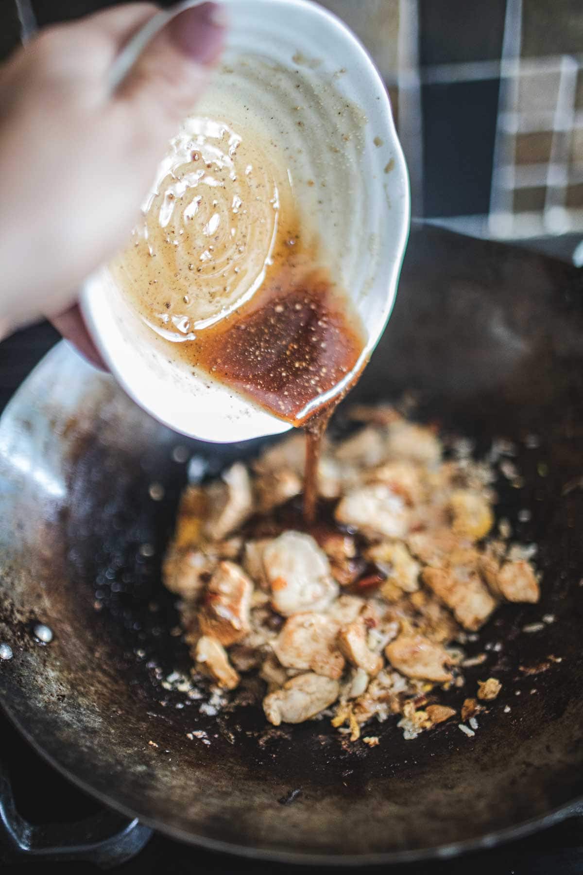 Sauce pouring over chicken in a wok.