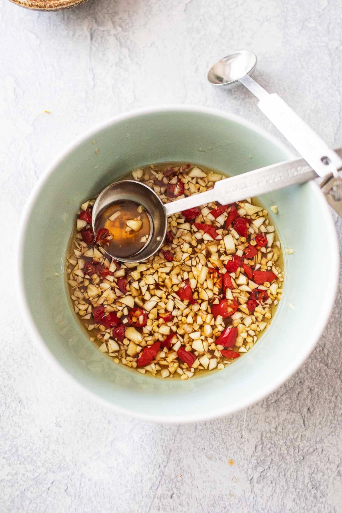 Ingredients for Nam Prik Pla sauce mixed in a bowl with measuring spoons. 