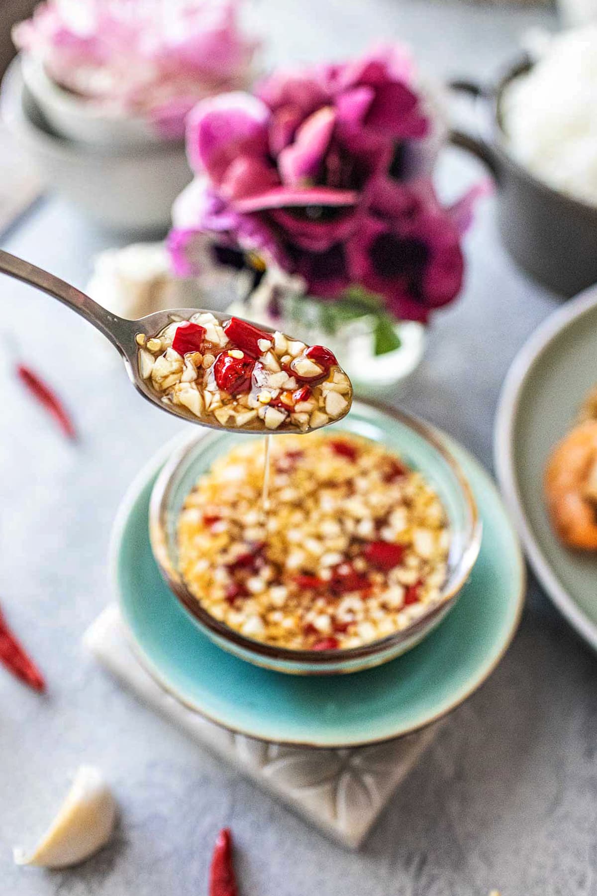 Spoon lifting and dripping Thai chili sauce from a bowl. 