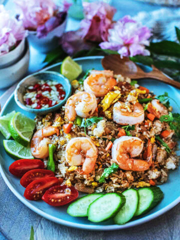 Thai shrimp fried rice on a plate with garnishes and flowers on the side.