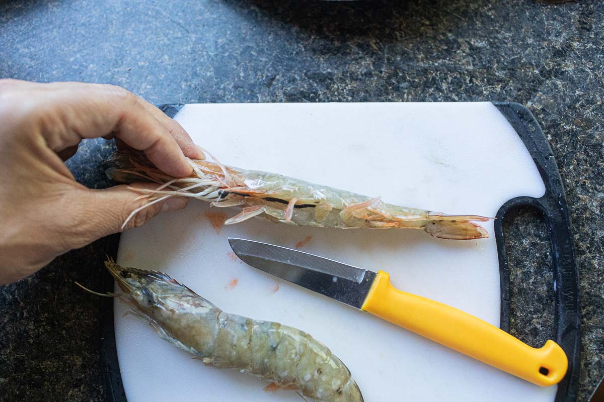 Deveining shrimp on a cutting board with a parring knife. 