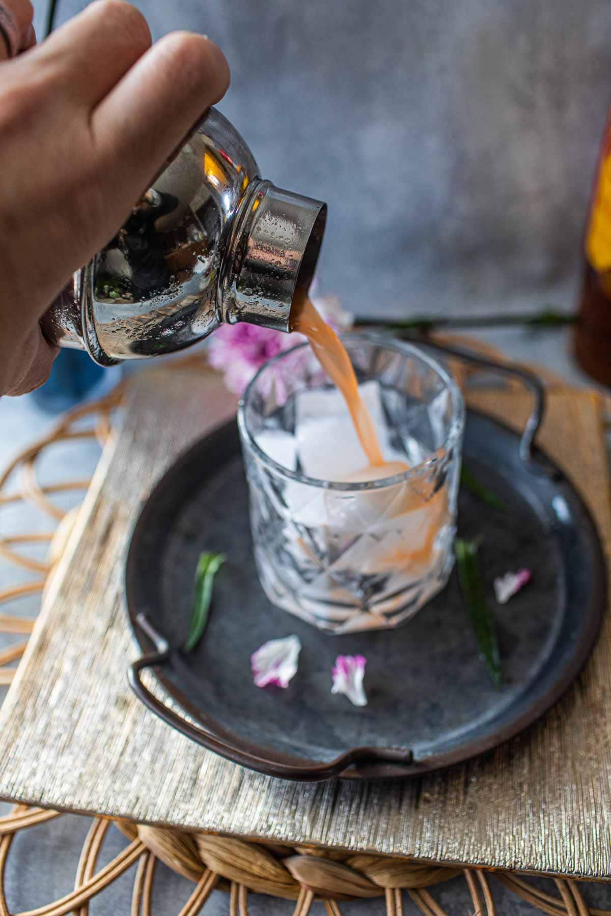 Mekhong whiskey sour pouring from shaker into a glass.