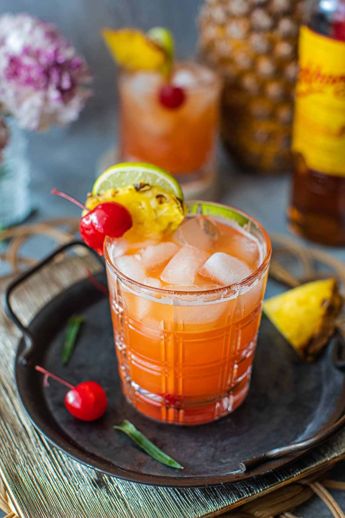 Mekhong whiskey sour in a glass with pineapple, lime and cherry garnish. 