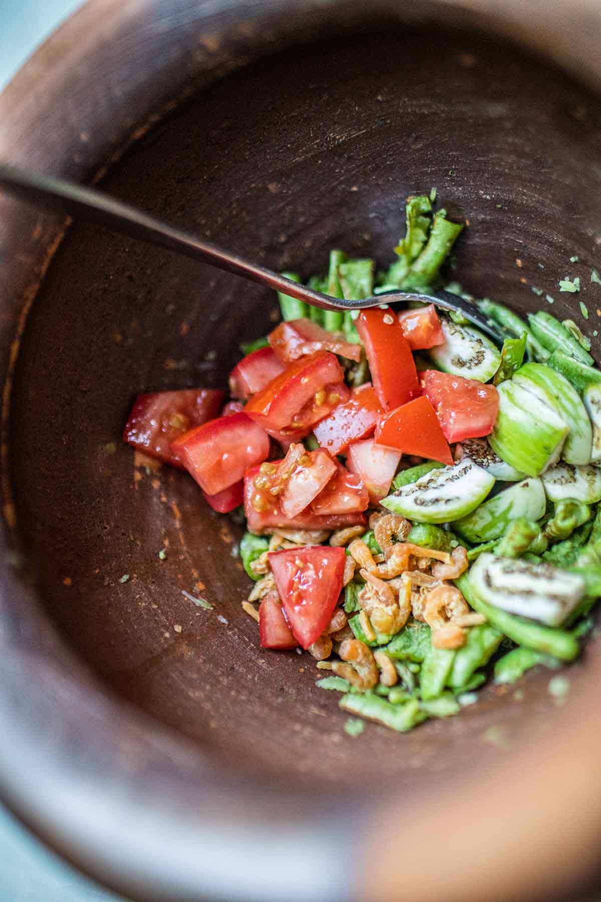 Tomatoes, dried shrimp and beans in a mortar. 