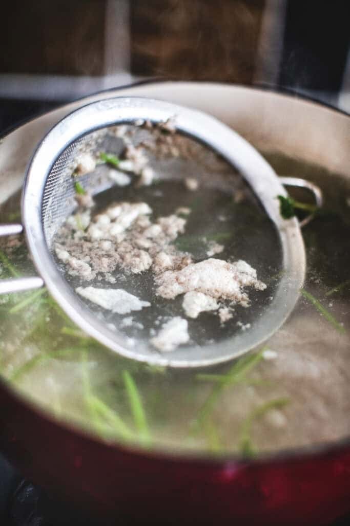 Spoon scooping soup scum from a pot.