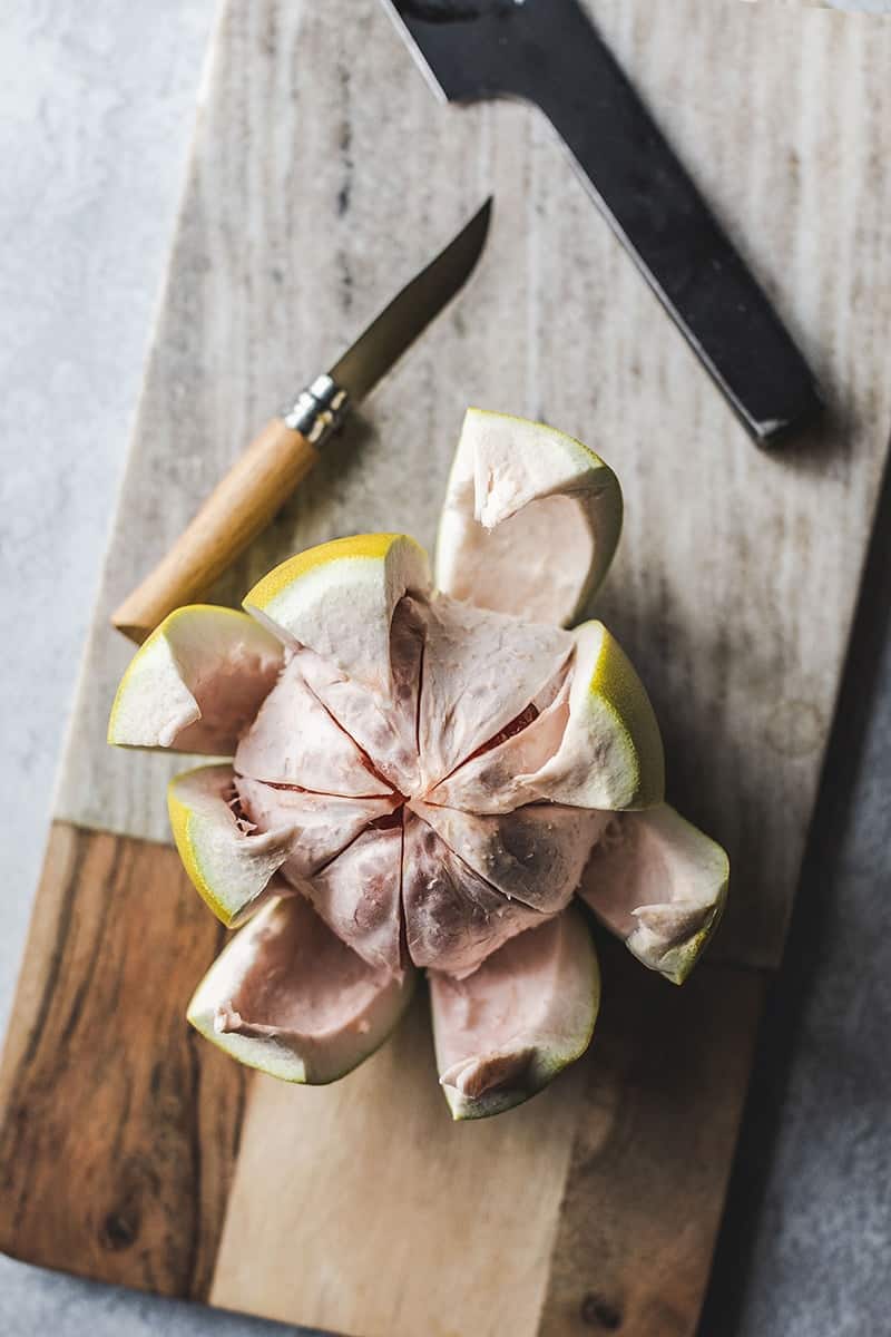 Pomelo sliced open in a bowl on a cutting board. 