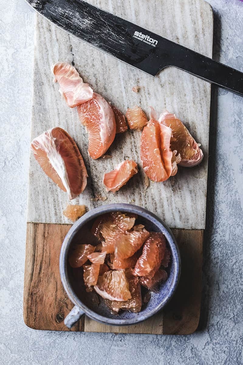 Pomelo slices in a bowl on a cutting board. 