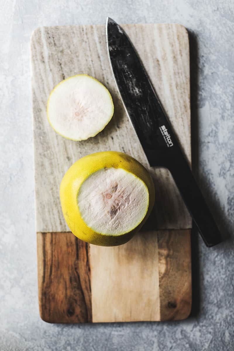 Knife with a pomelo on a cutting board.