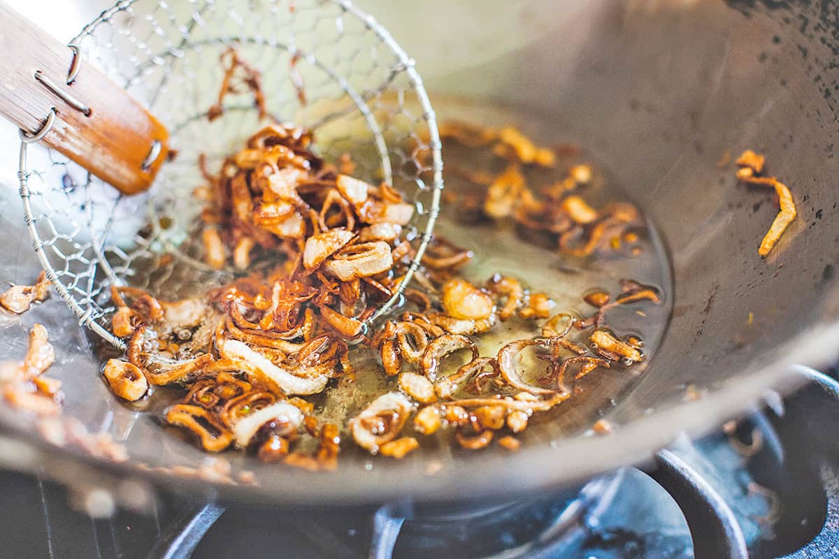 Crispy fried shallots in a wok with slotted spoon.