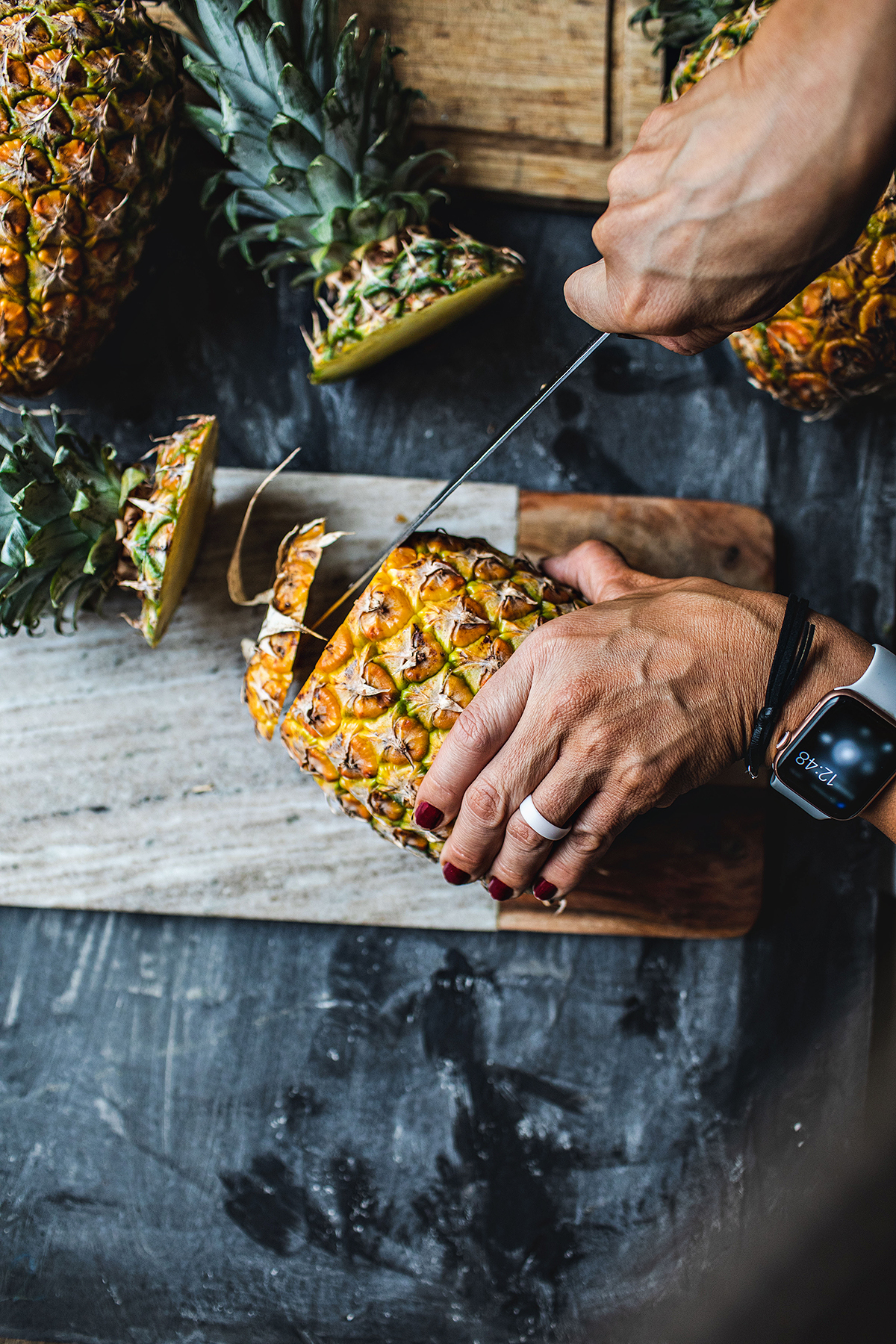 A hand and knife cutting pineapple.