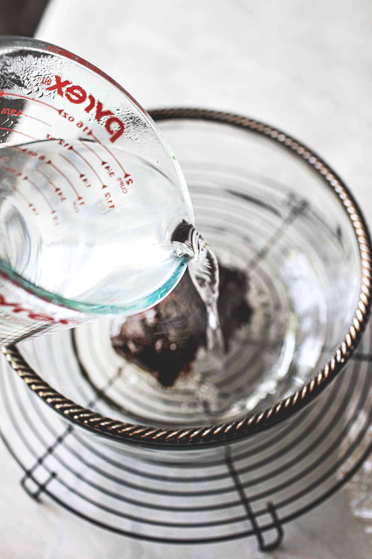 Hot water pouring over Tamarind paste in a glass bowl.